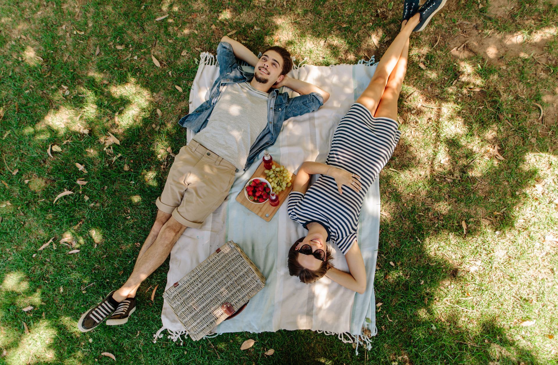 Couple relaxing on a picnic blanket under a tree in a park.