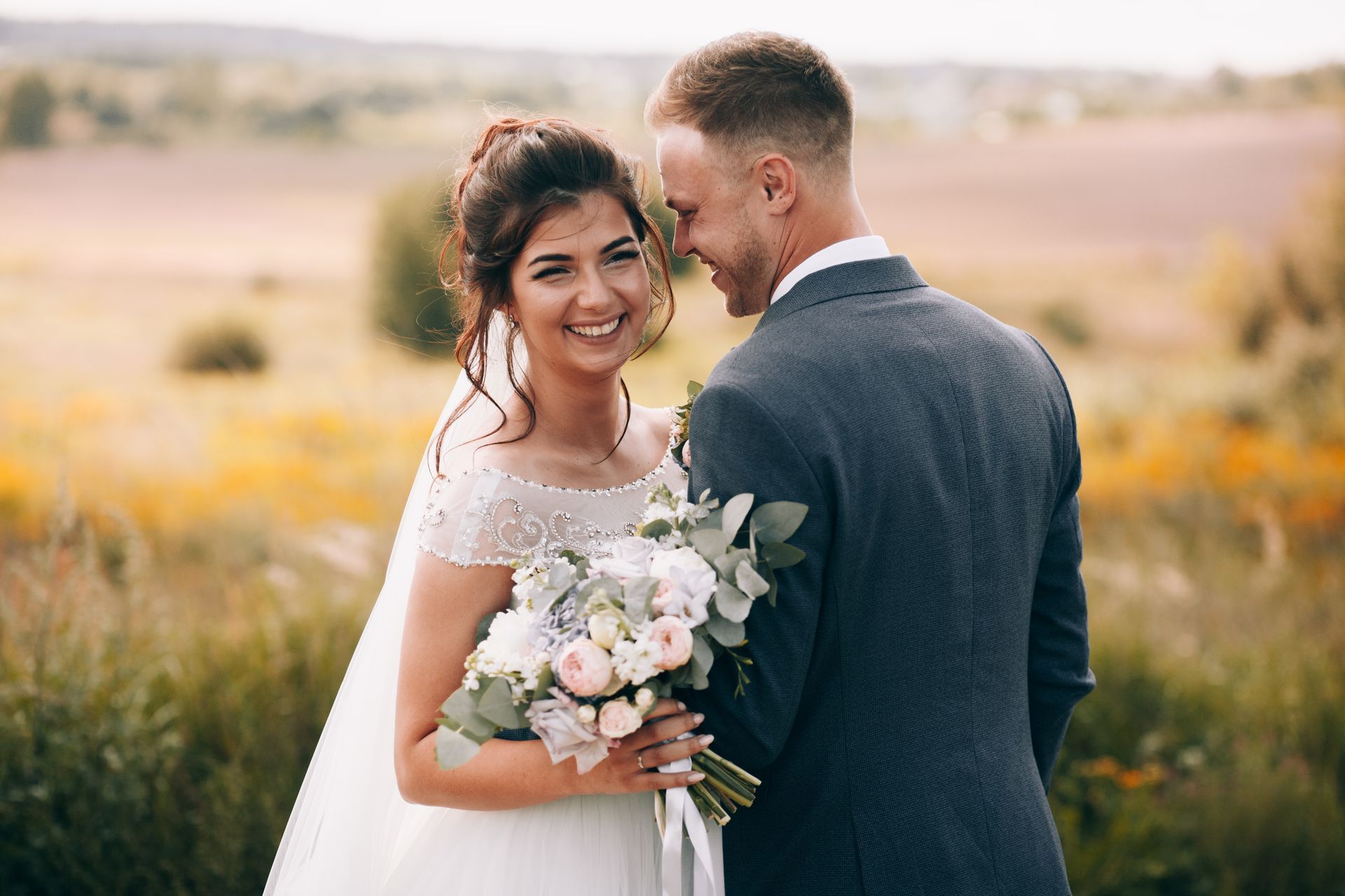 A bride and groom are posing for a picture in a field on their wedding day.