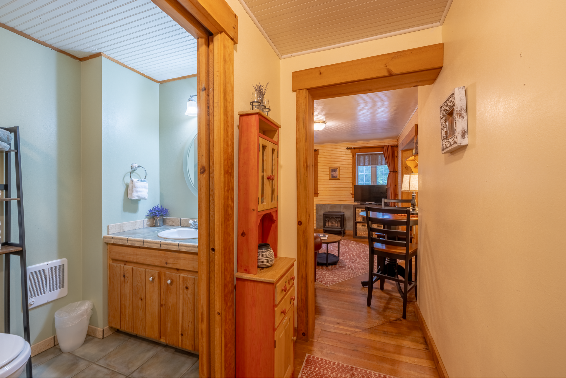 View down a hallway with doorways to a bathroom (left) and living area (right). The bathroom has a light blue wall and wooden vanity.