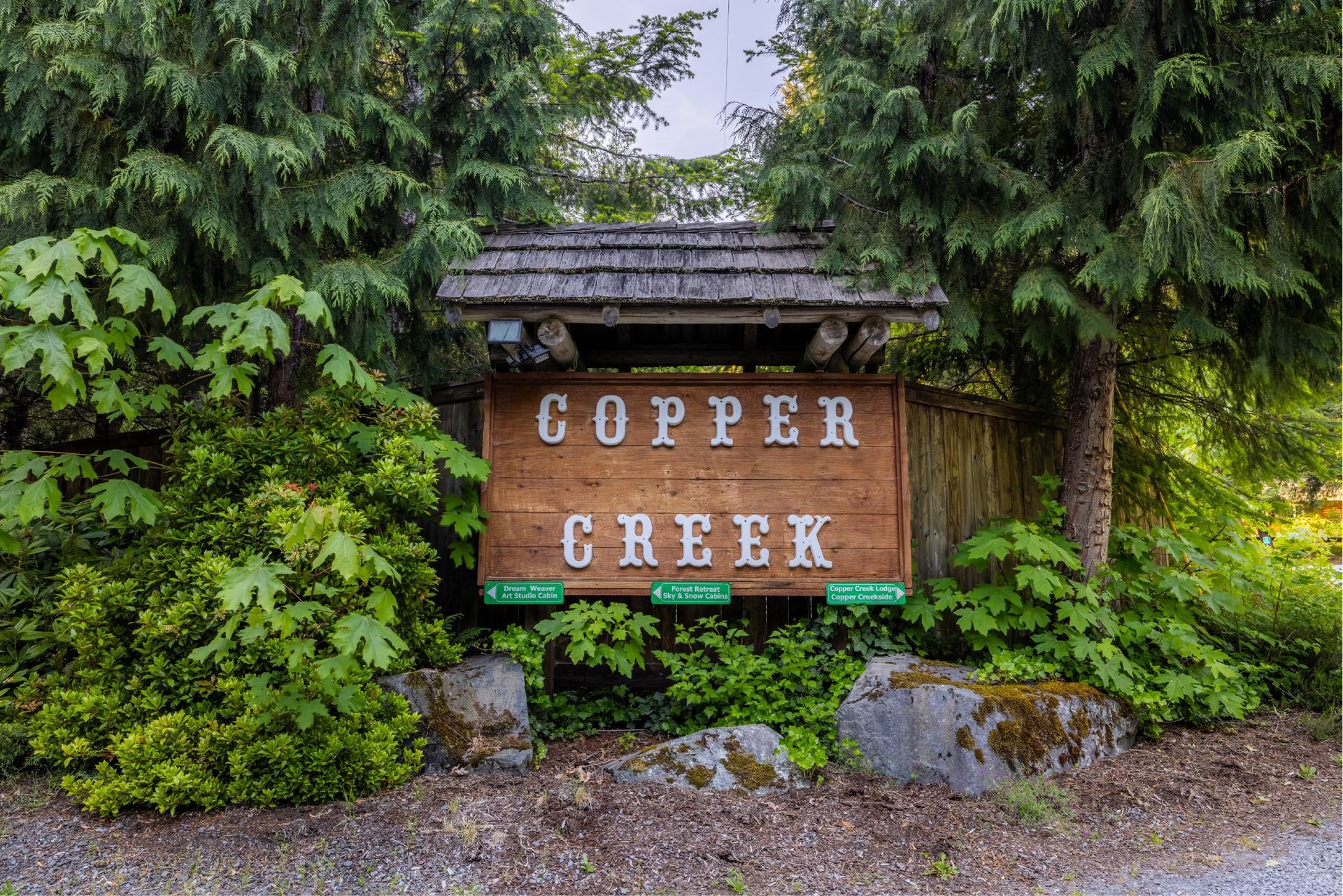 Sign for Copper Creek, made of brown wood with white lettering, surrounded by greenery and trees.