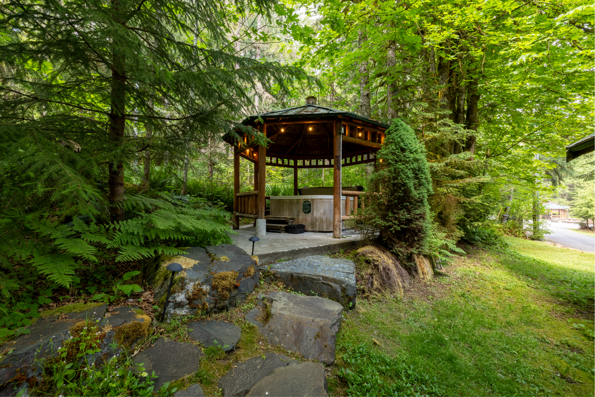 A wooden gazebo with a green roof in the middle of a forest
