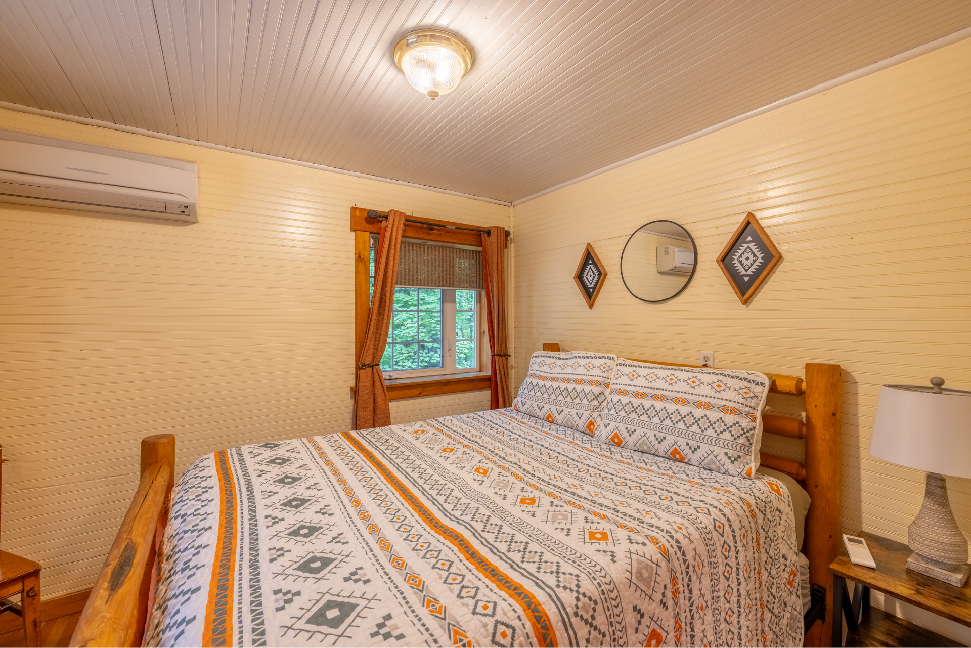 Bedroom with wooden bed frame, patterned bedding, window with curtains, and decorative wall accents.