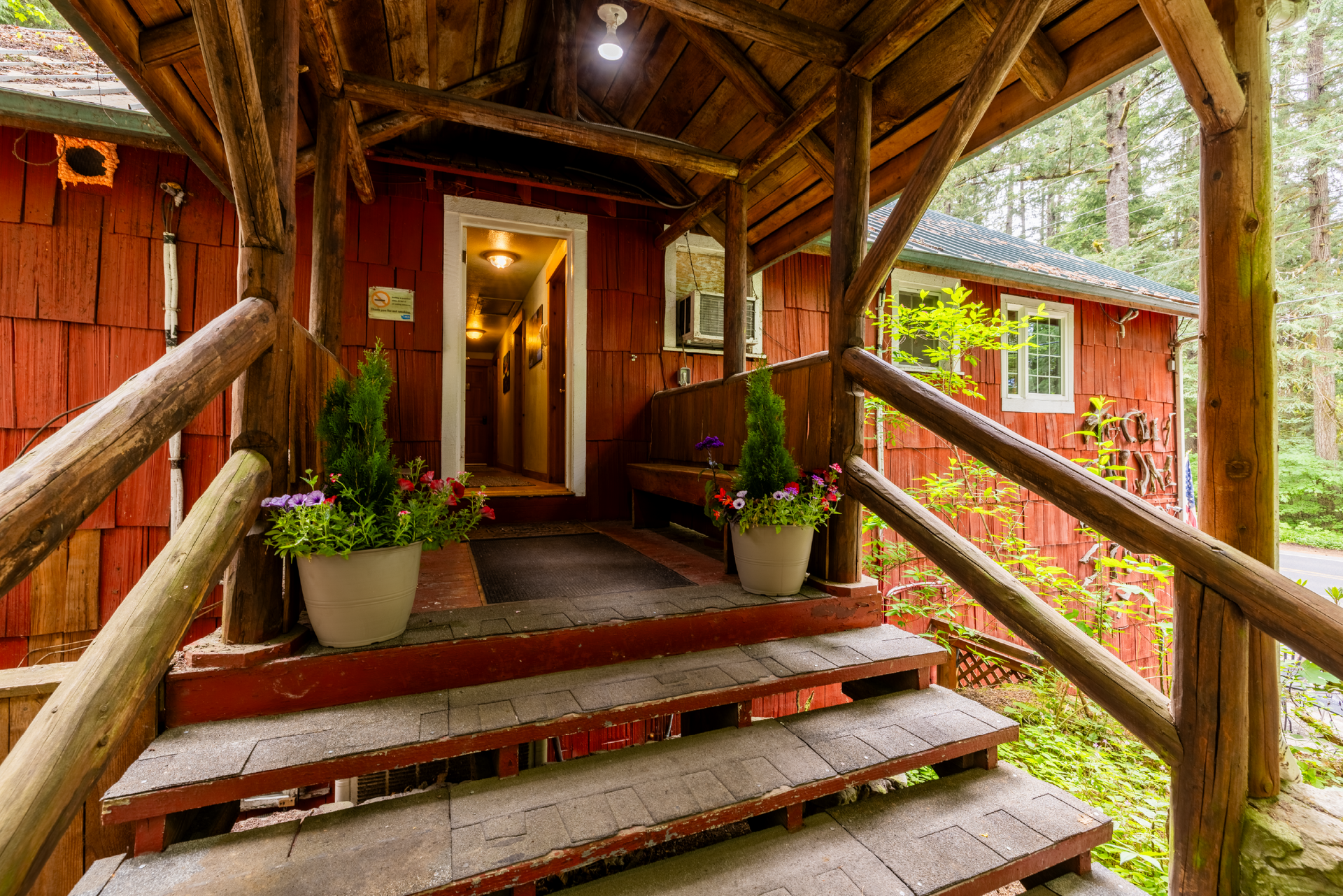 Red wooden cabin entrance with steps, porch, and potted plants. Interior hallway visible through open door.