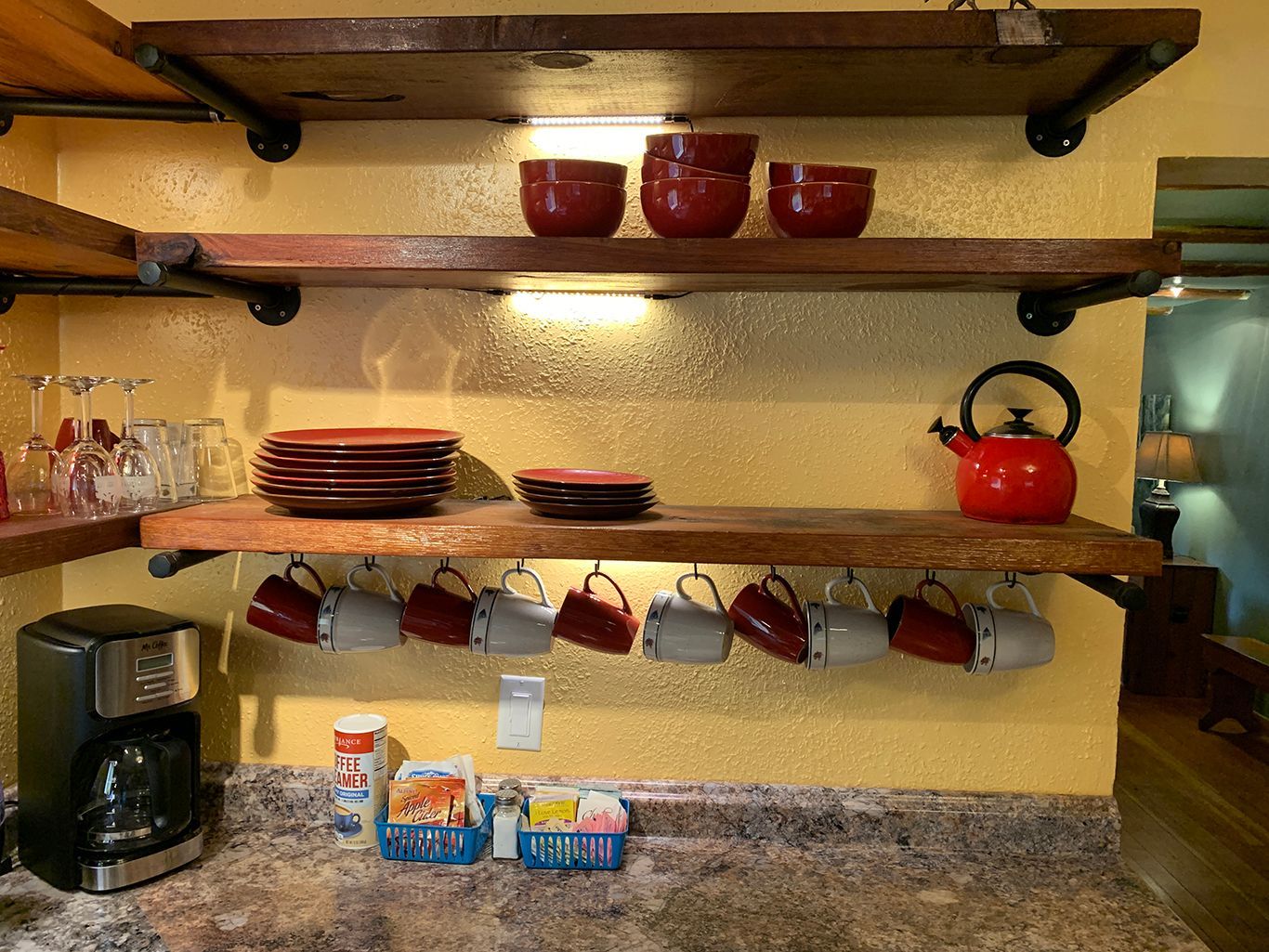 A kitchen with a coffee maker , plates , cups , and a kettle on the shelves.