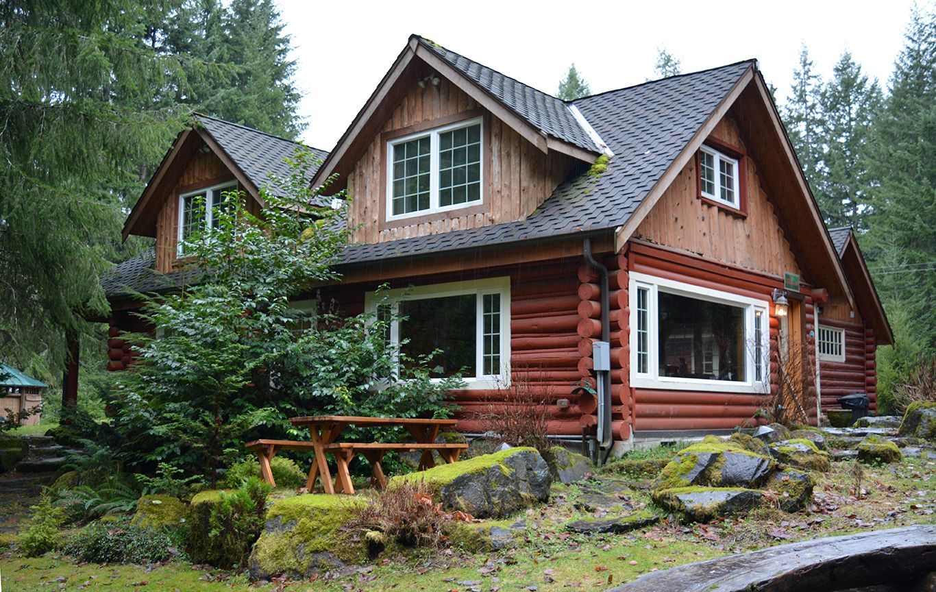 A log cabin in the middle of a forest with a picnic table in front of it.