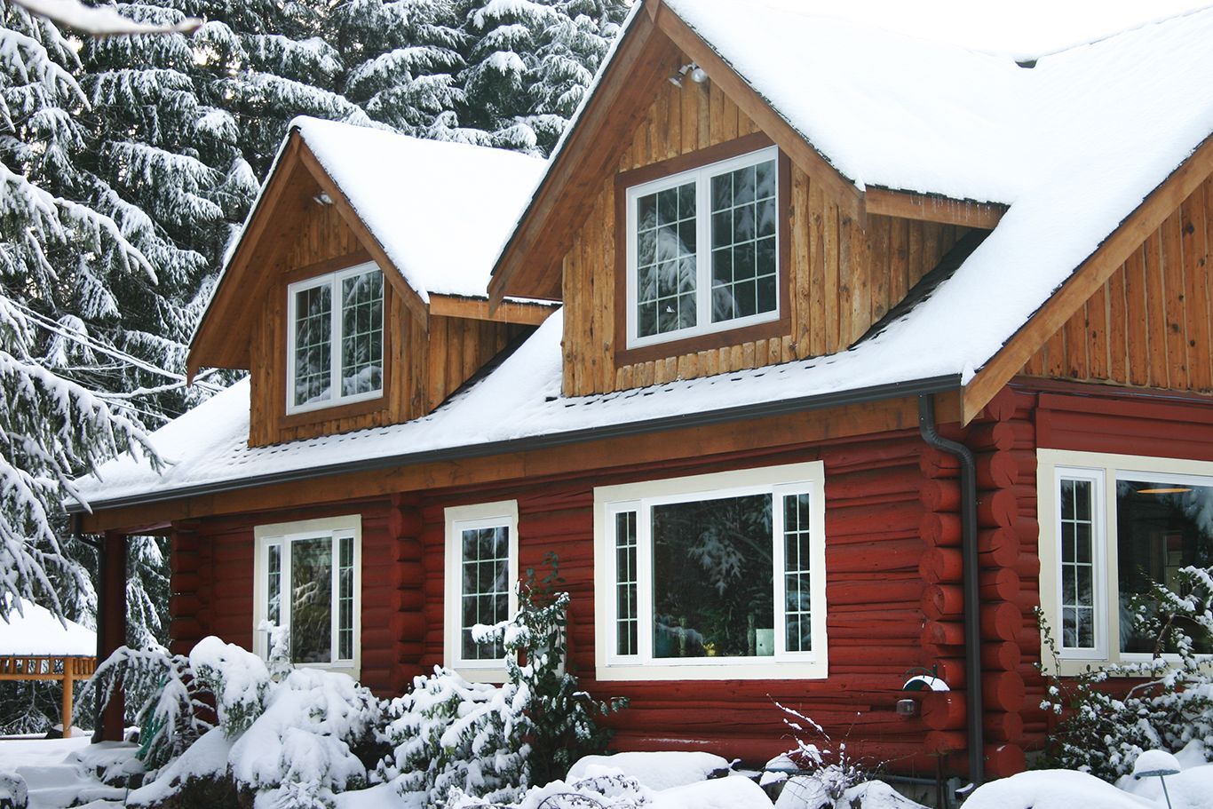 A red log cabin covered in snow with trees in the background