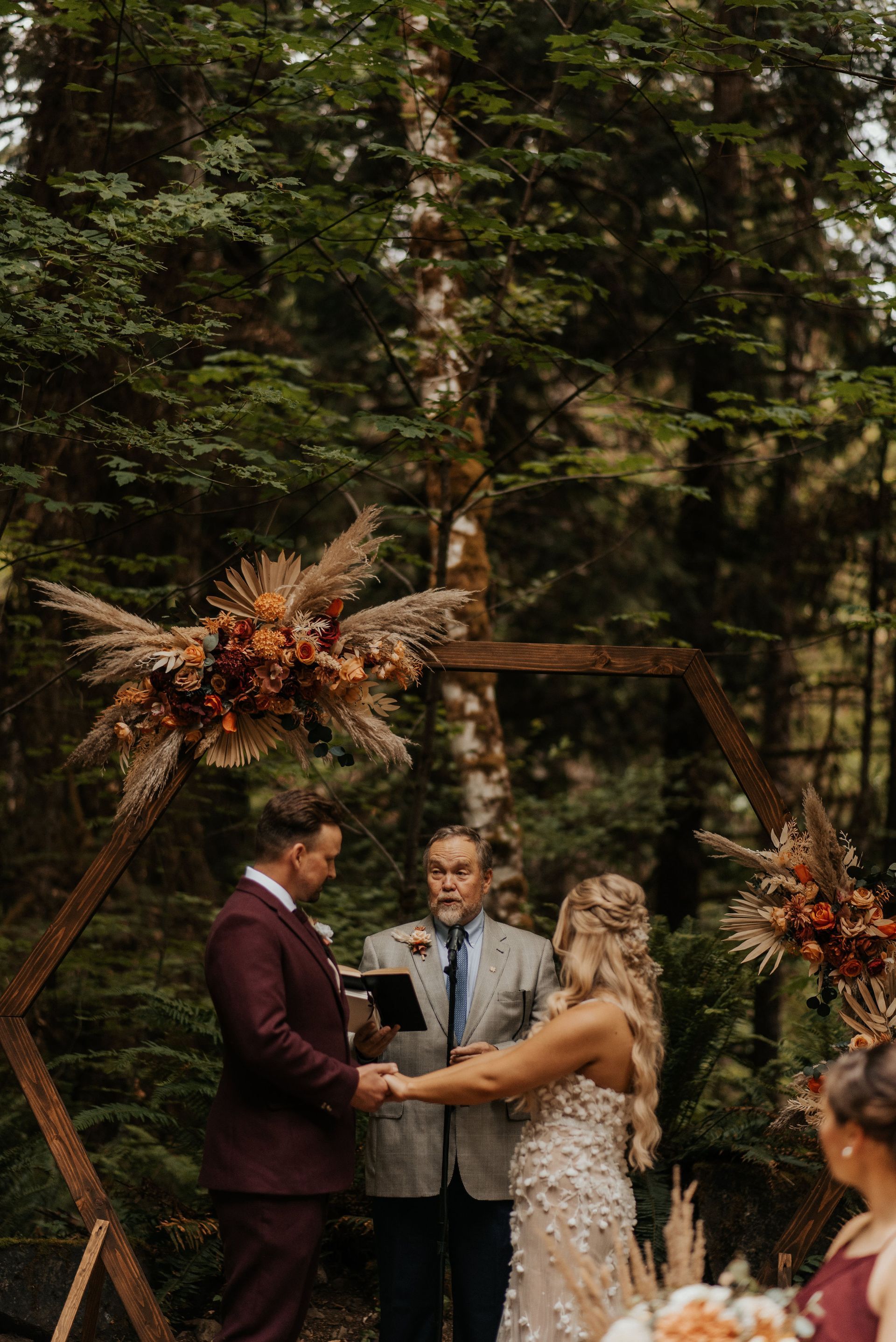 A bride and groom are holding hands during their wedding ceremony in the woods.