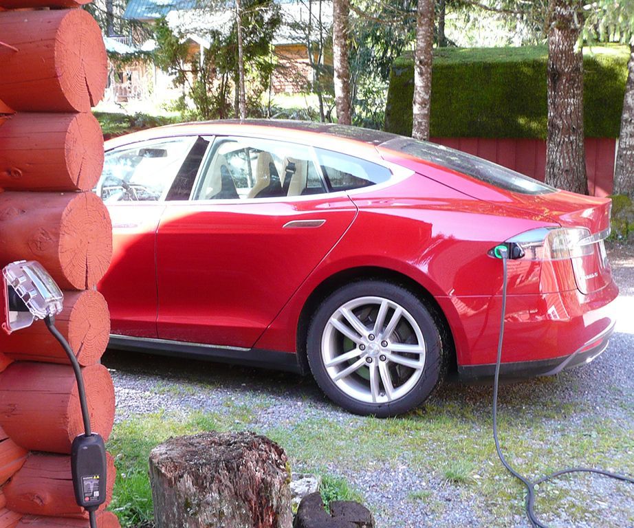 A red tesla model s is charging in front of a log cabin