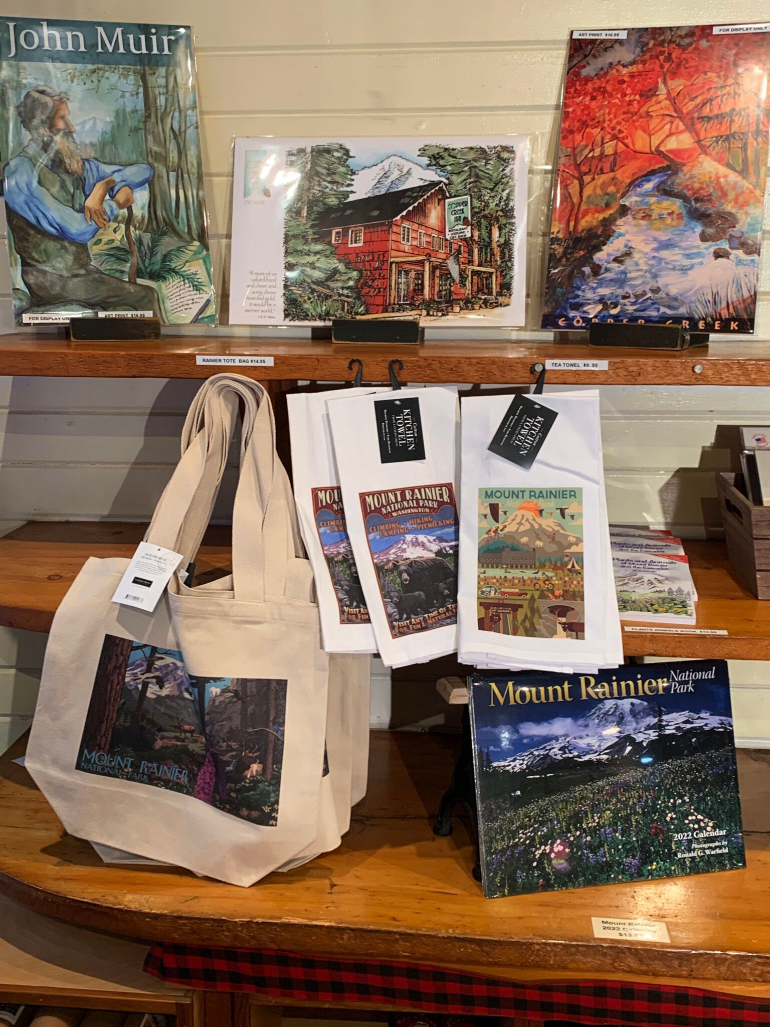 A display of paintings and a tote bag on a wooden shelf.
