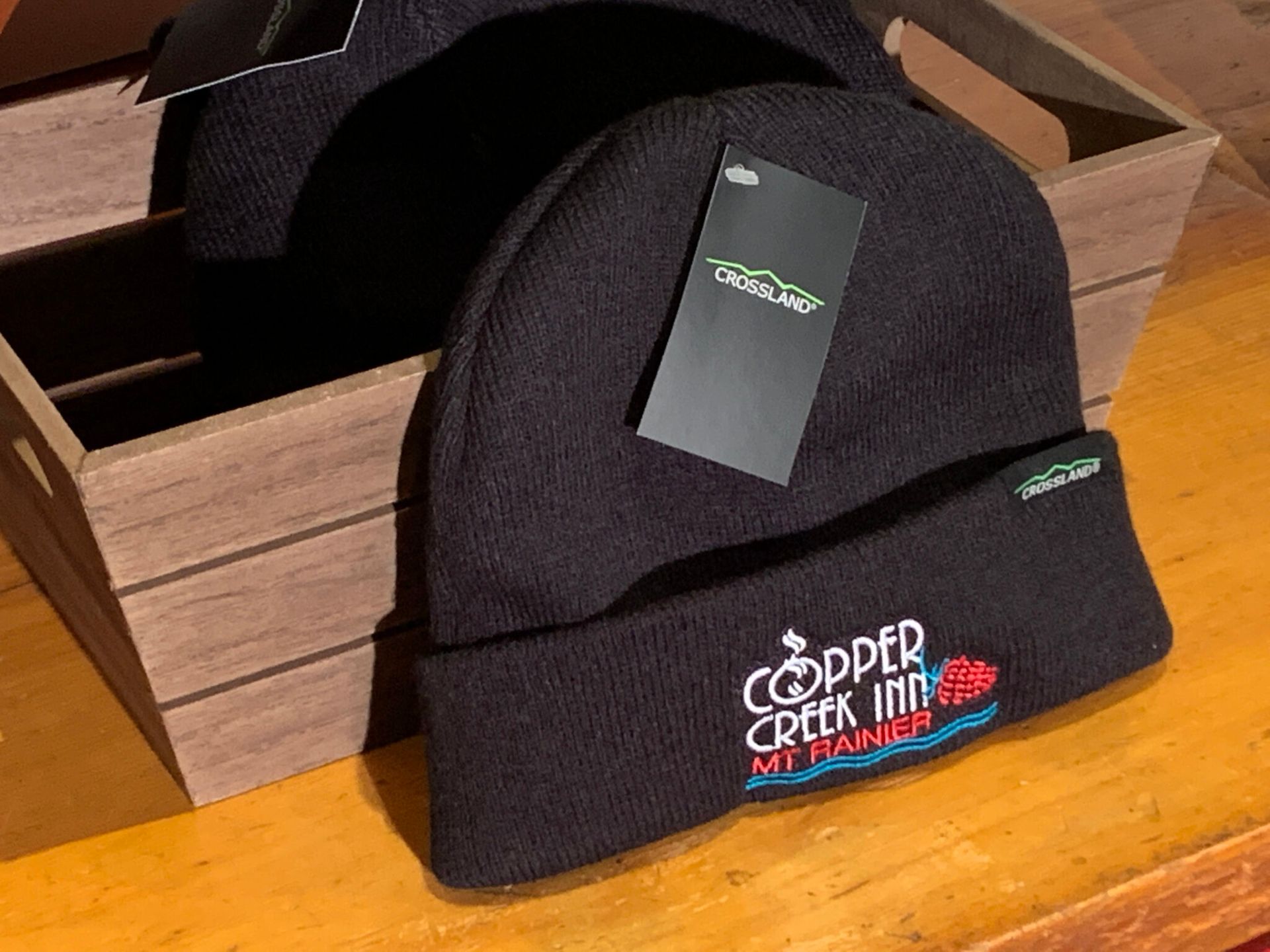 A black beanie is sitting on a wooden table next to a wooden box.