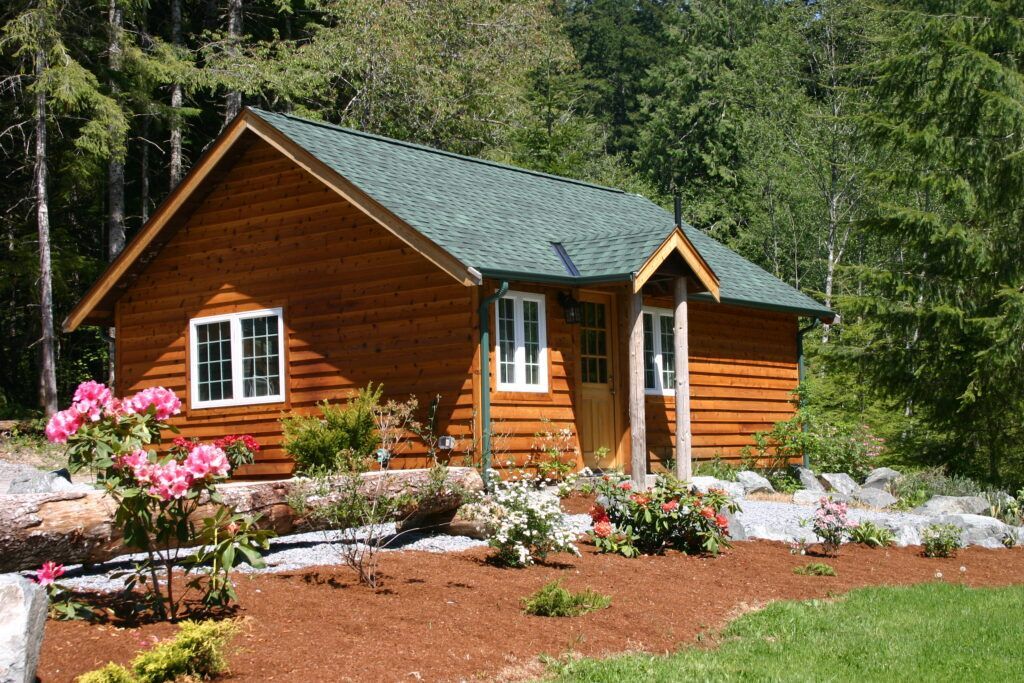 A small log cabin with a green roof is surrounded by trees