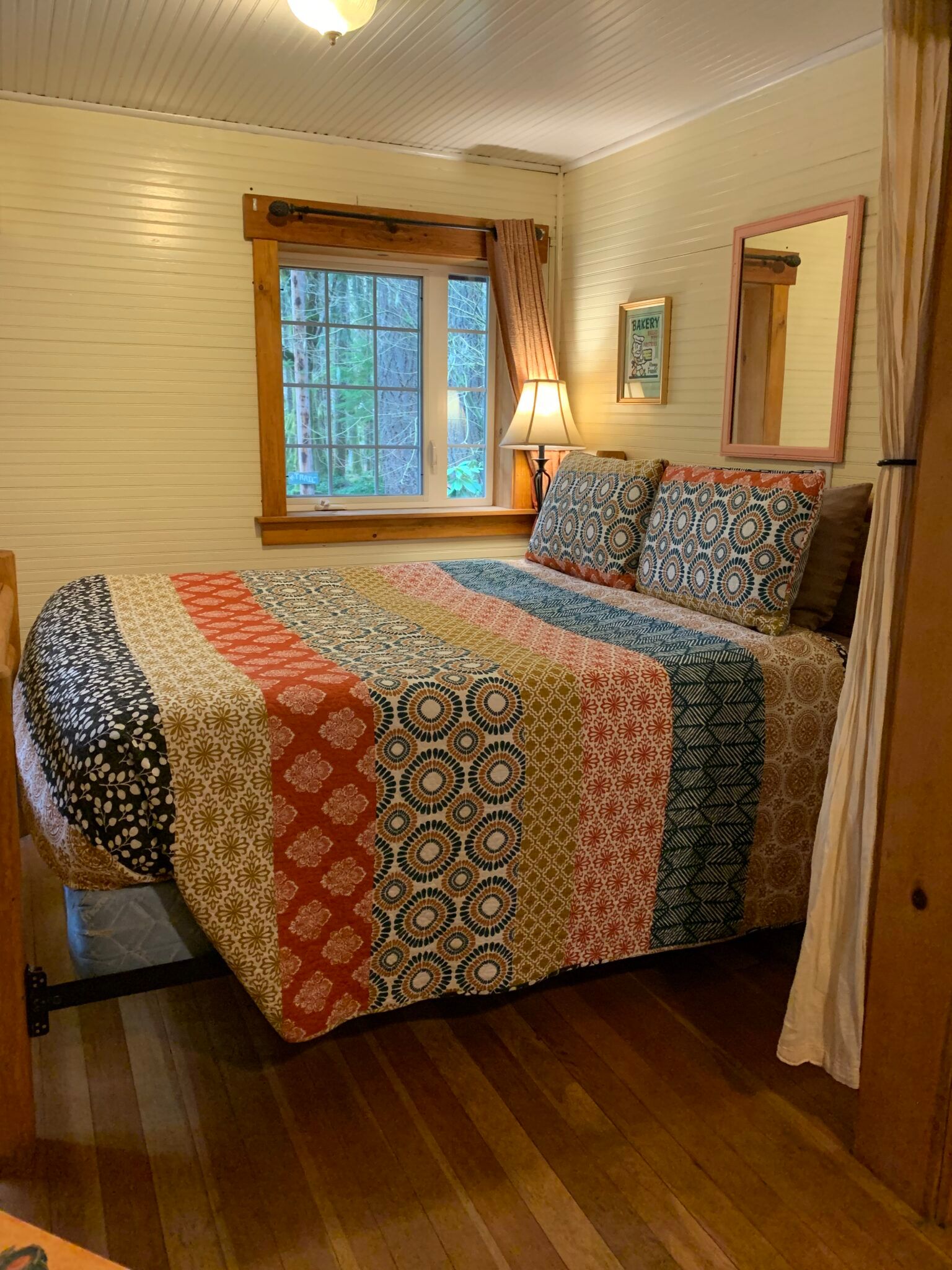 A bedroom with a bed , lamp , mirror and window.