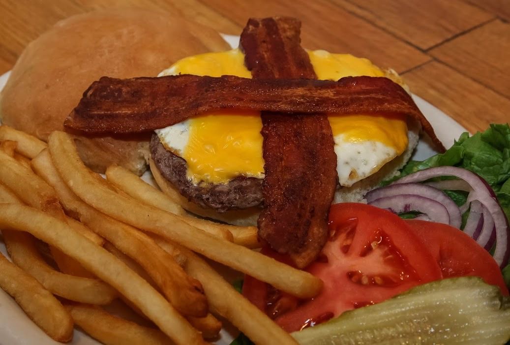 A hamburger with bacon and french fries on a plate