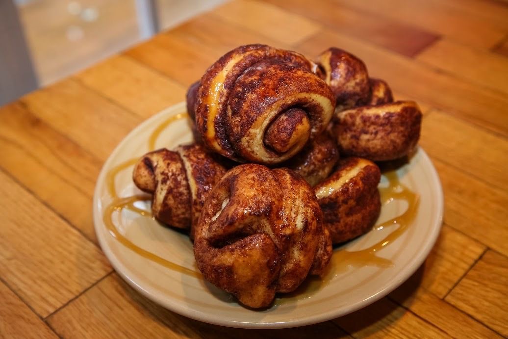 A plate of cinnamon rolls with syrup on a wooden table.