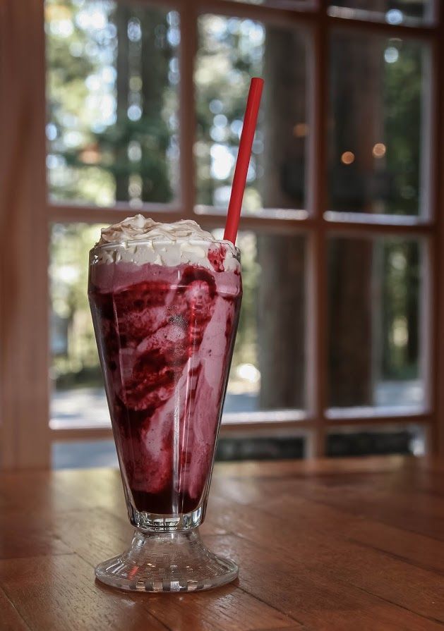 A milkshake with whipped cream and a red straw on a table in front of a window.