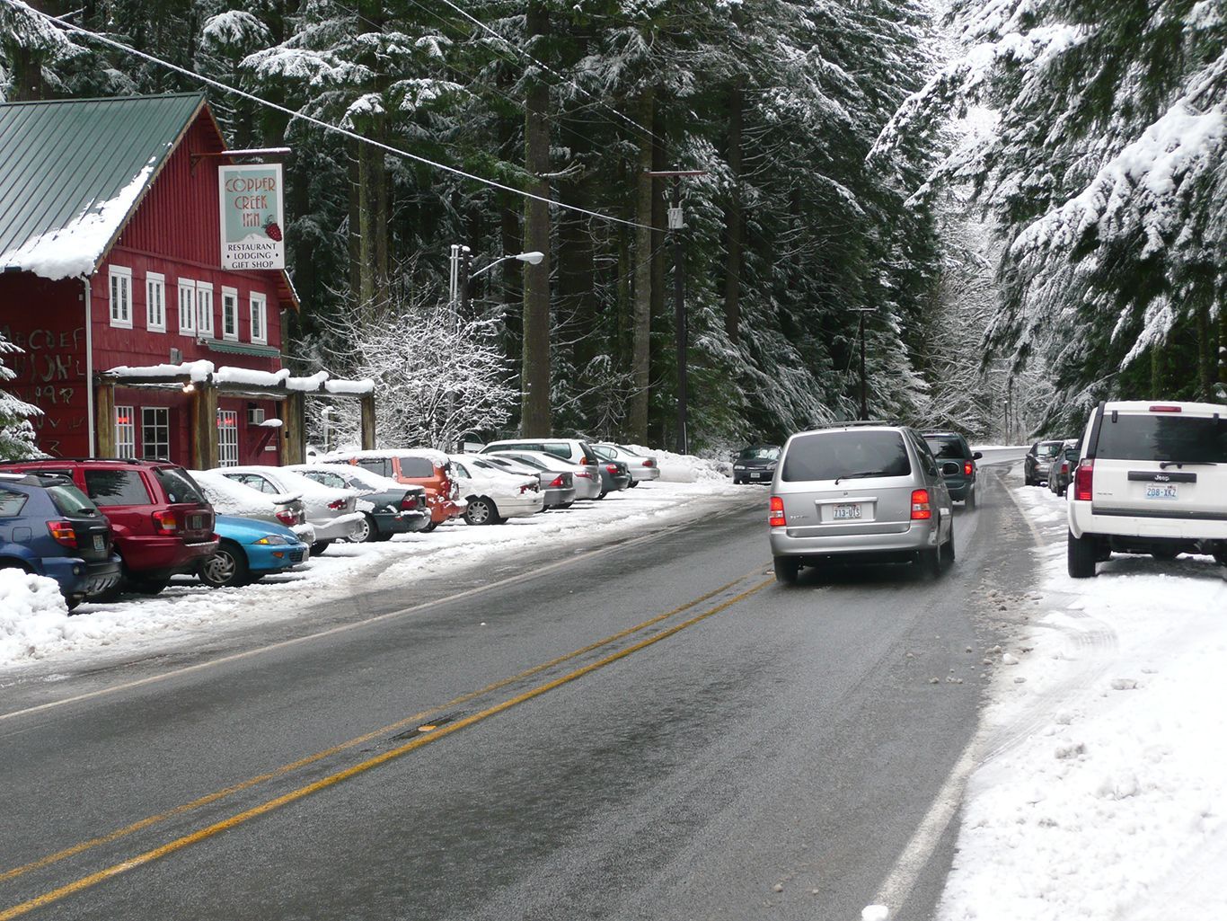 A row of cars are parked on the side of a snowy road