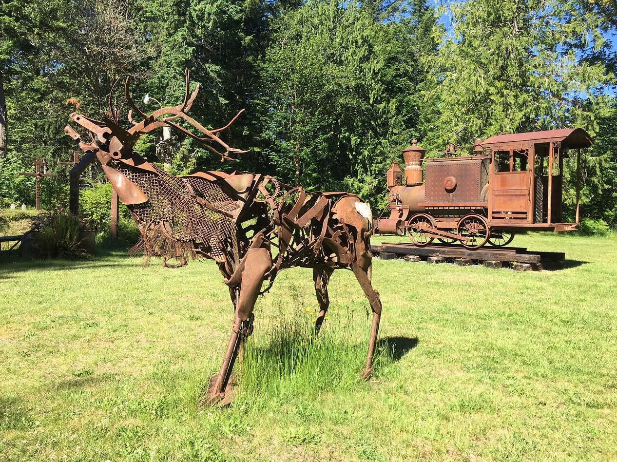 A statue of a deer and a train in a field.