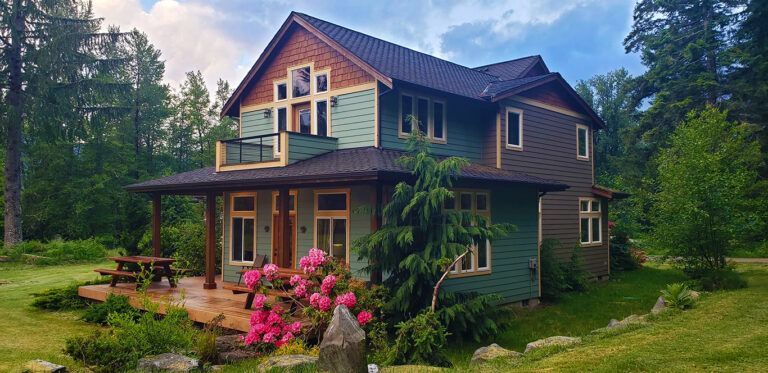 A large green house with a porch in the middle of a forest.