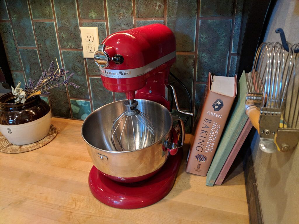 A red kitchenaid mixer is sitting on a wooden counter next to a book.