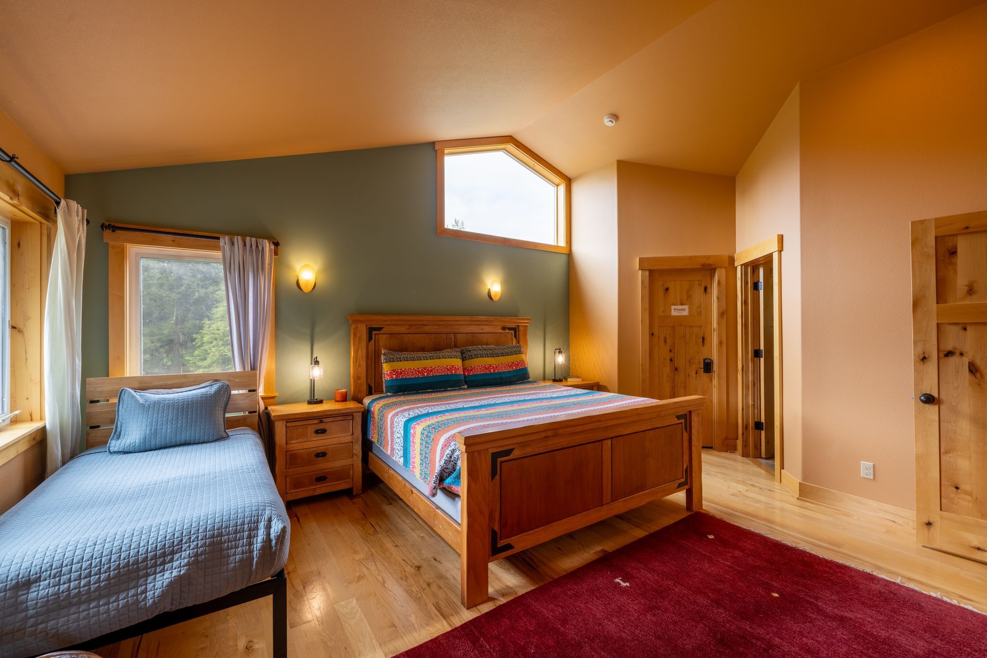 Bedroom with a queen bed, a twin bed, wood floors, and a red rug. Walls are peach and teal.
