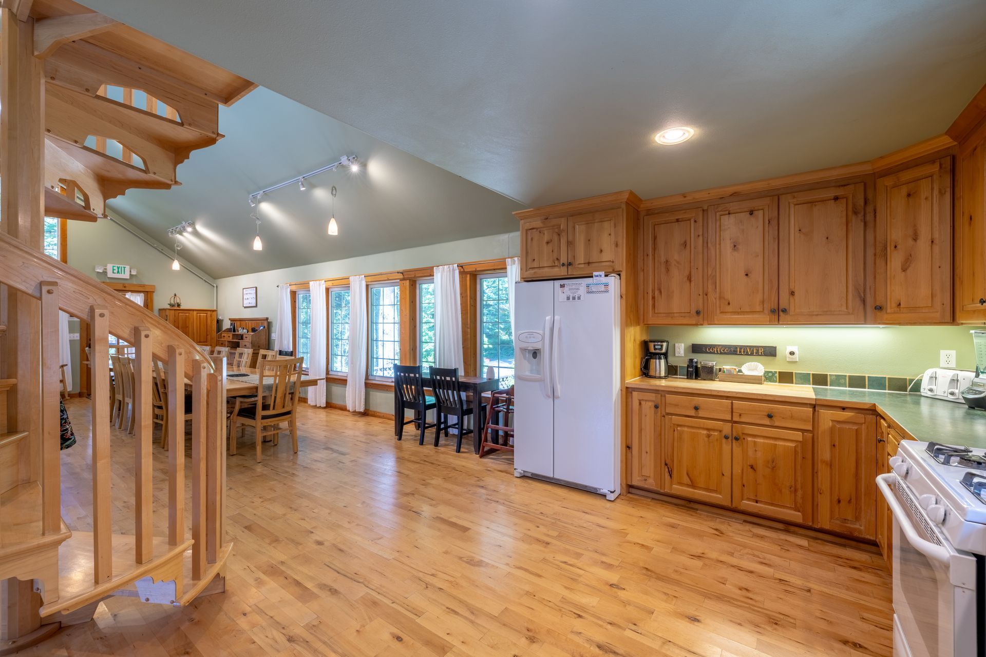 Open-plan kitchen and dining area with wooden cabinets, light-colored hardwood floors, and a staircase.