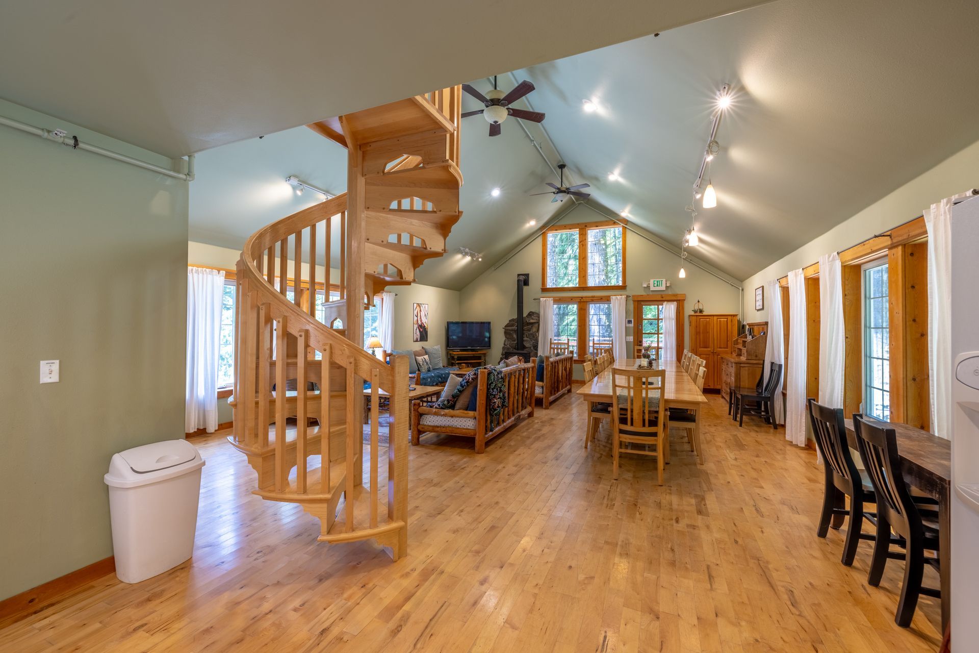 A spacious interior with wooden spiral staircase, light wood flooring, and a long dining table. The room has high ceilings and natural light.