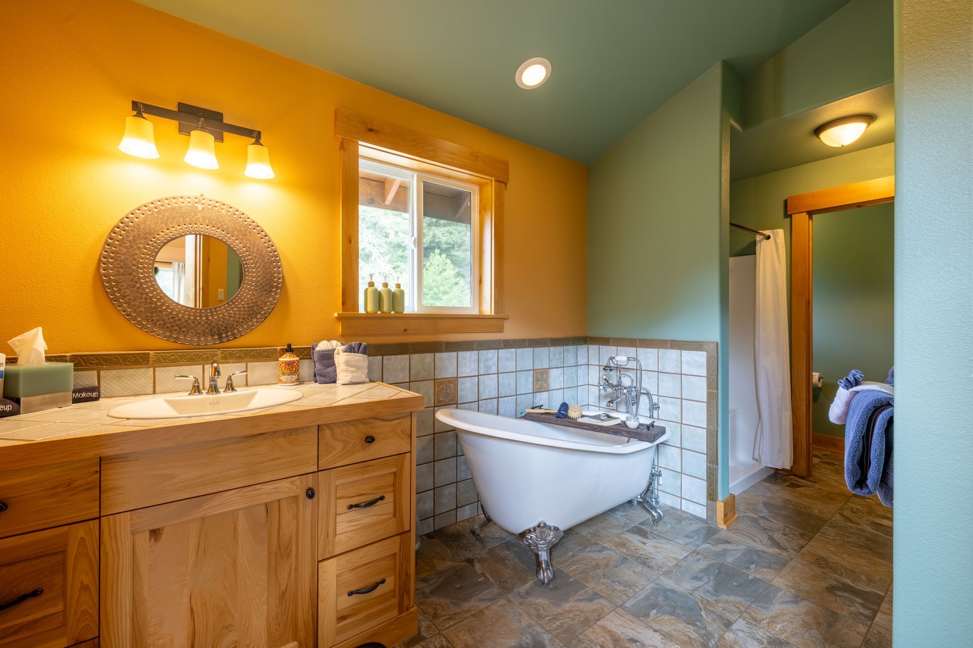 A bathroom with a claw-foot tub, wooden vanity, and a window, with colorful walls in yellow and green.