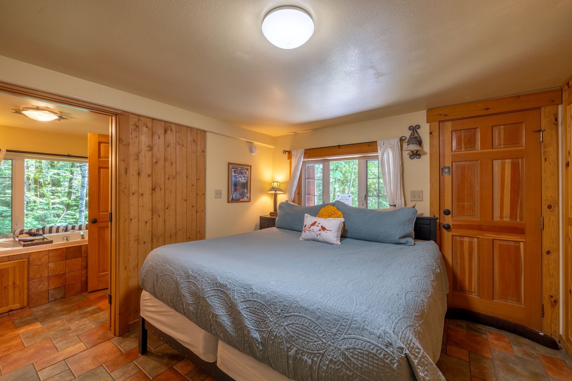 Bedroom with a king-size bed, wood-paneled walls and door, and a view of a bathroom and the outdoors.