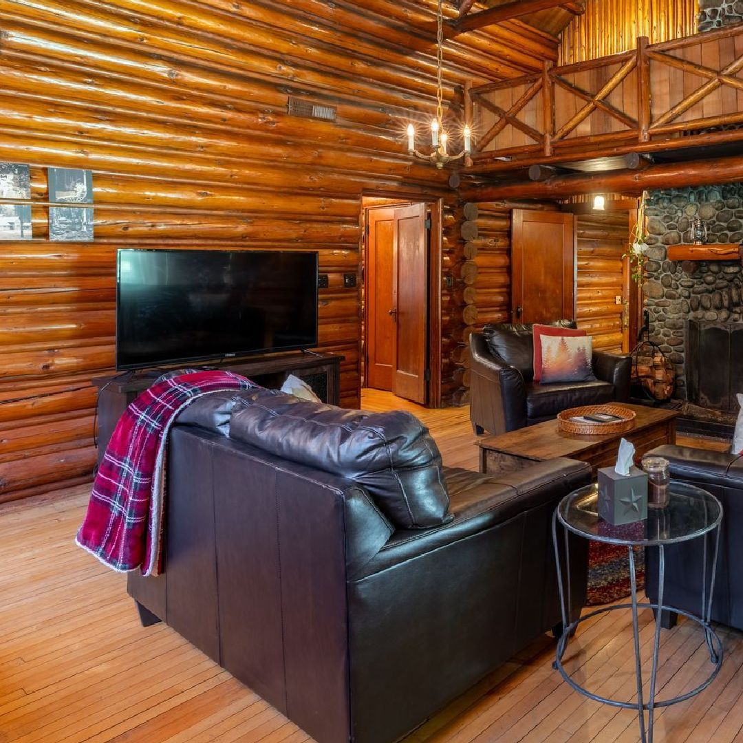 Cozy log cabin living room with leather sofas, fireplace, and TV; wooden walls and a loft area.