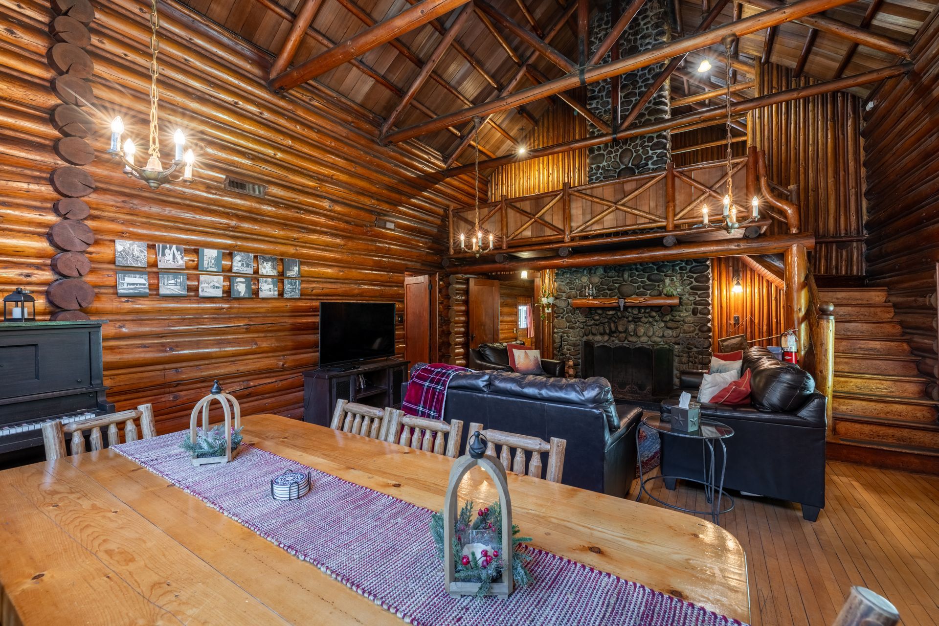 Rustic interior with log walls, a large dining table, and a living area with a fireplace and loft.