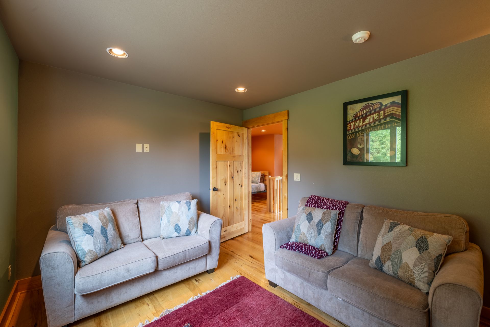 A cozy living area with two gray couches, a red rug, and a doorway leading to a bedroom.