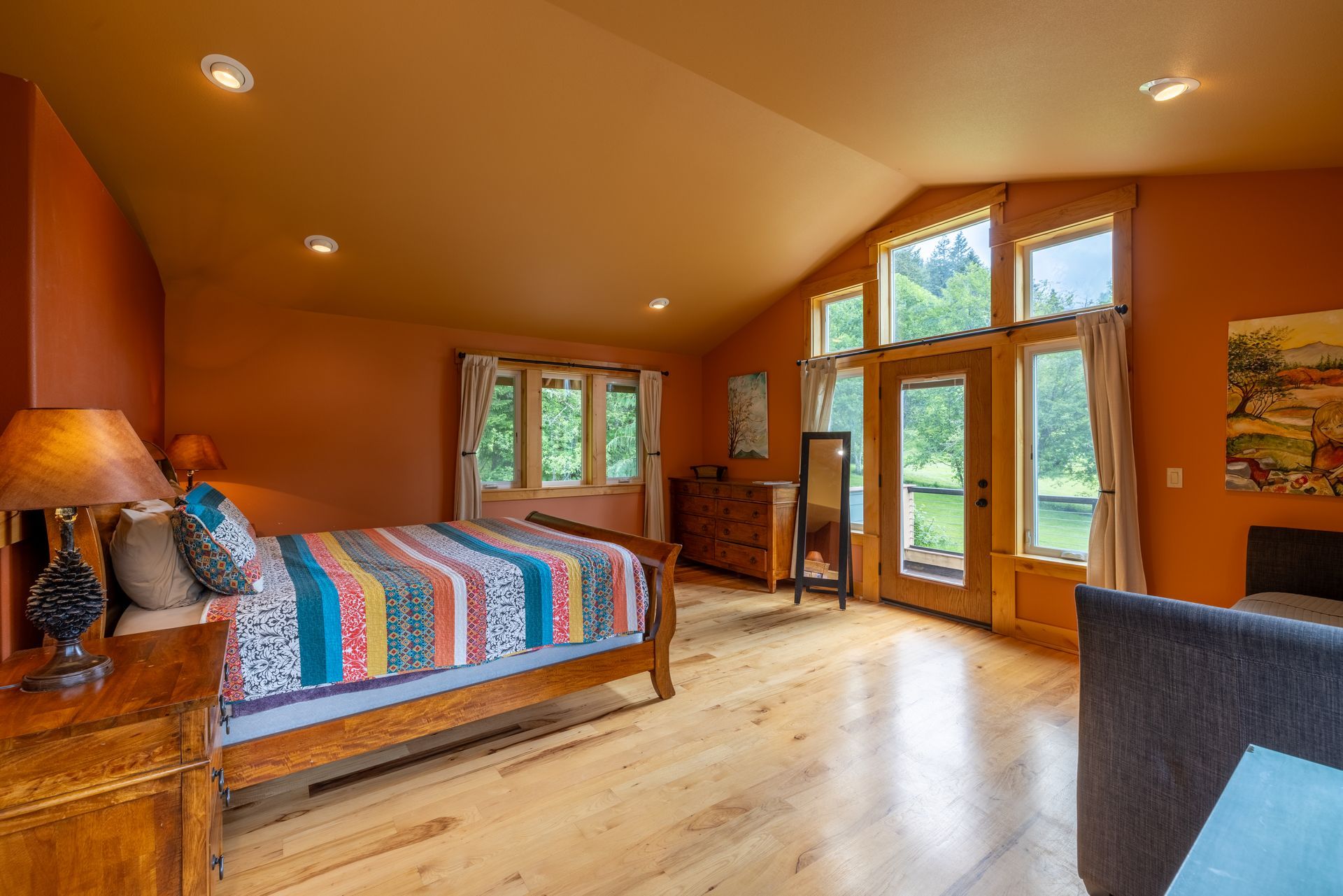 A bedroom with orange walls, a wooden bed with a colorful quilt, and a door to a green outdoor area.