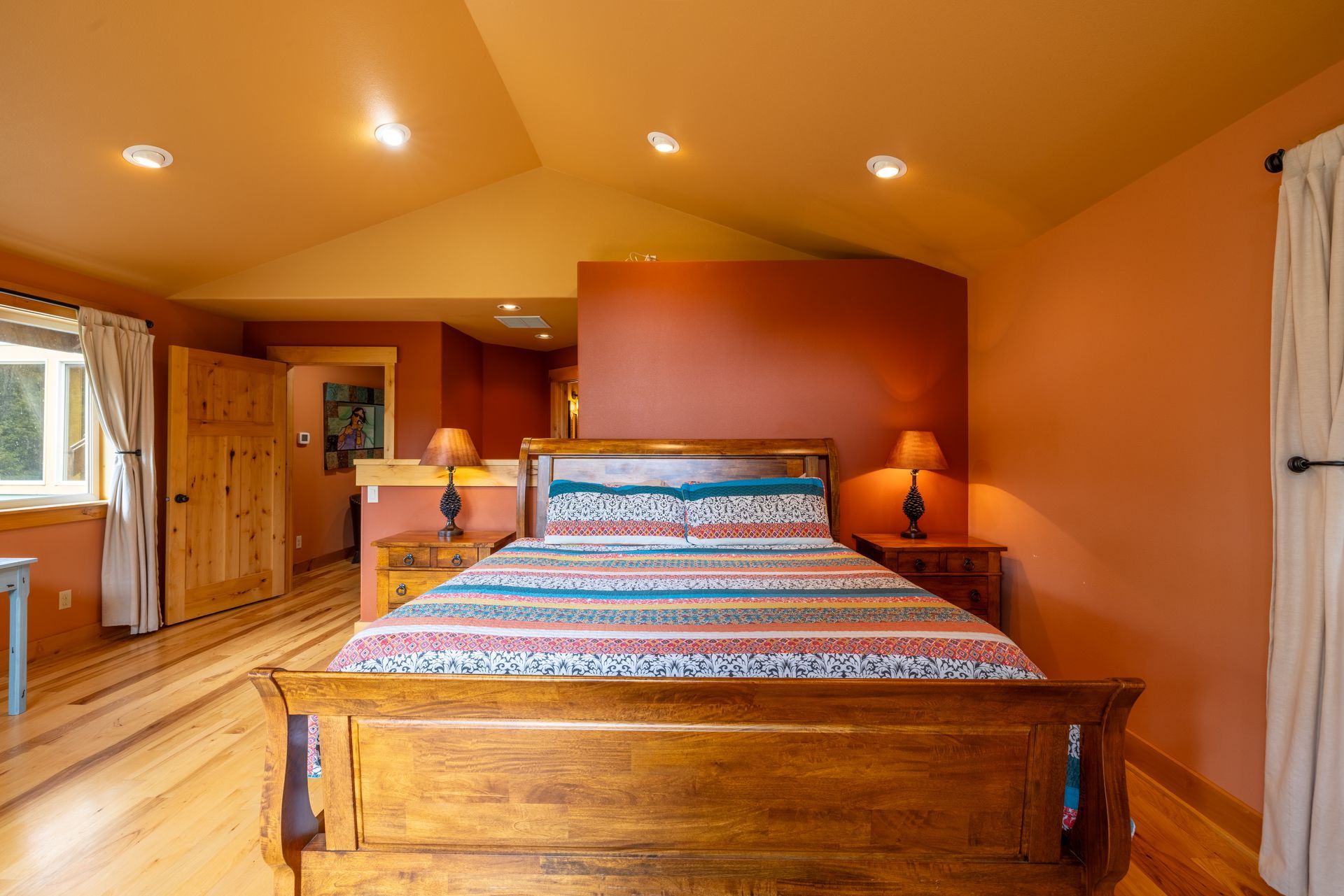 Bedroom with orange walls, wooden floor, and a wooden sleigh bed with patterned bedding.