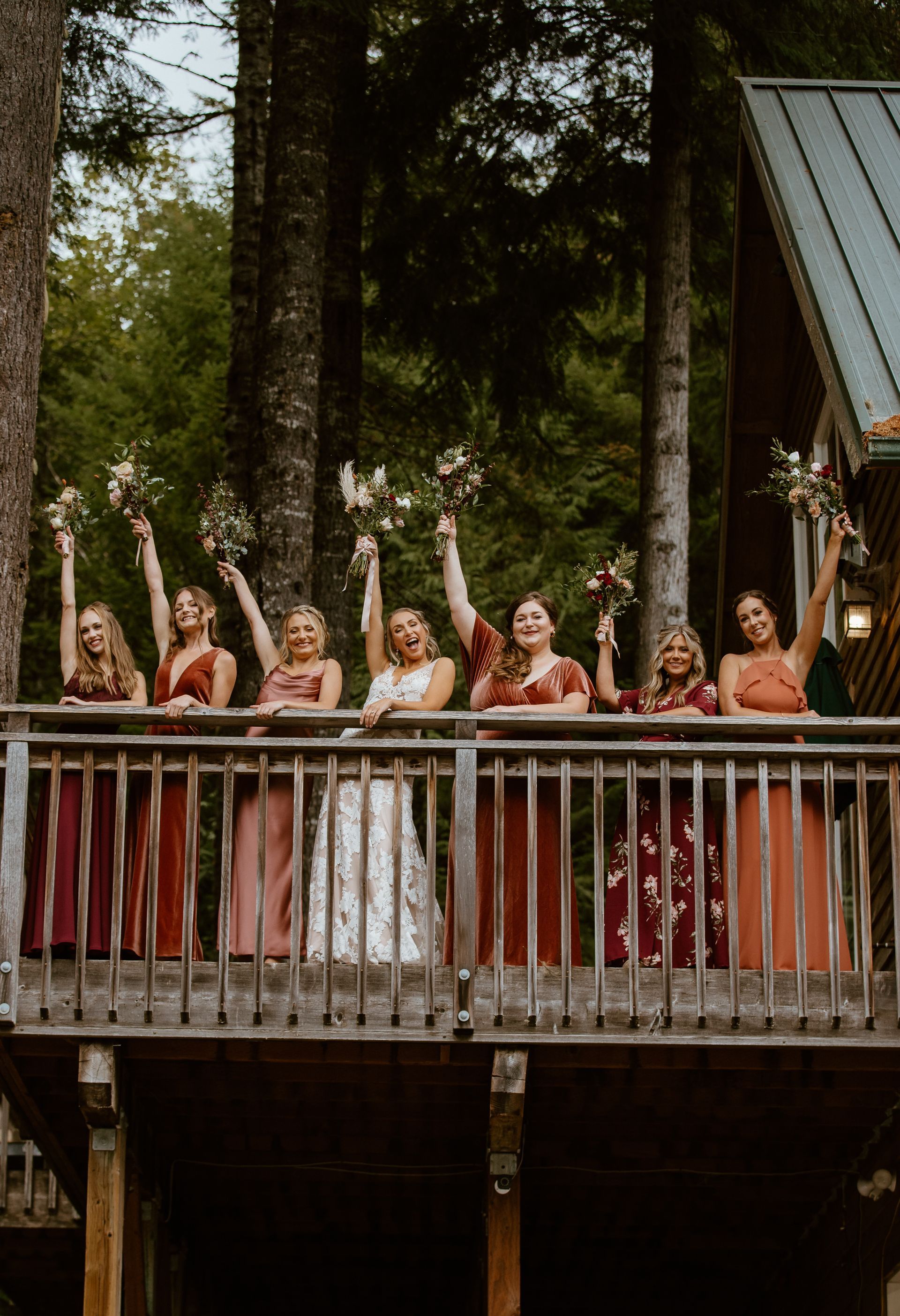 A bride and her bridesmaids are standing on a balcony holding their bouquets in the air.