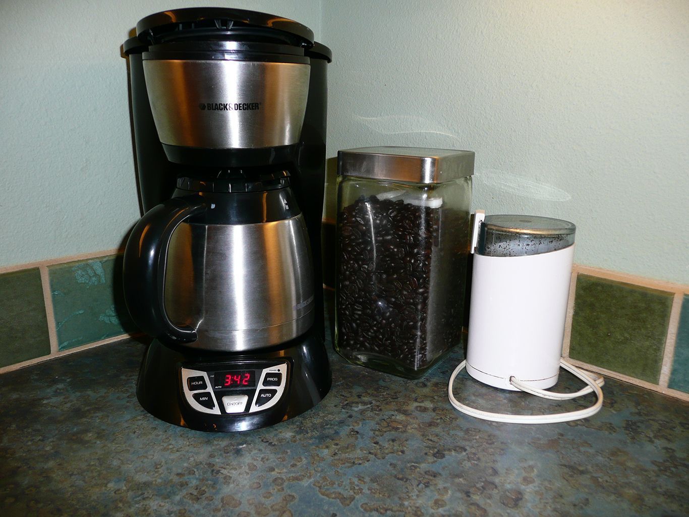 A black and silver coffee maker sits on a counter next to a jar of coffee beans