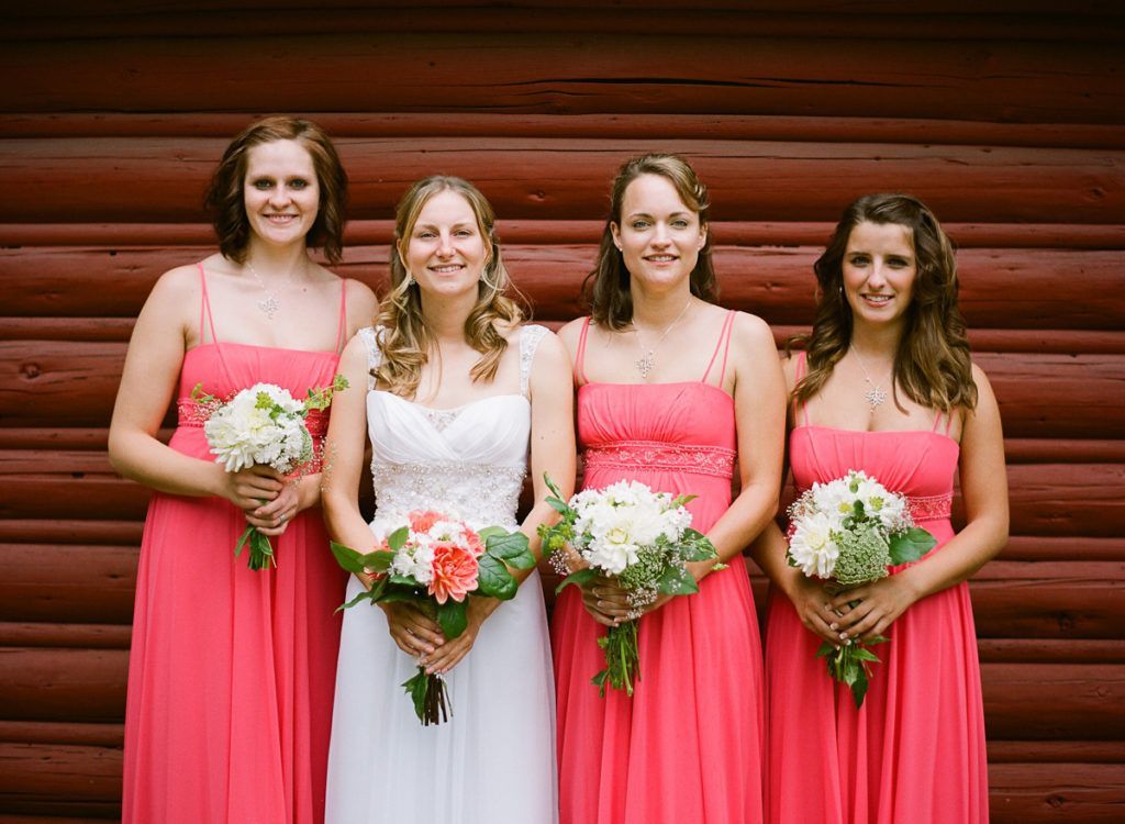 A bride and her bridesmaids are posing for a picture in front of a log cabin.