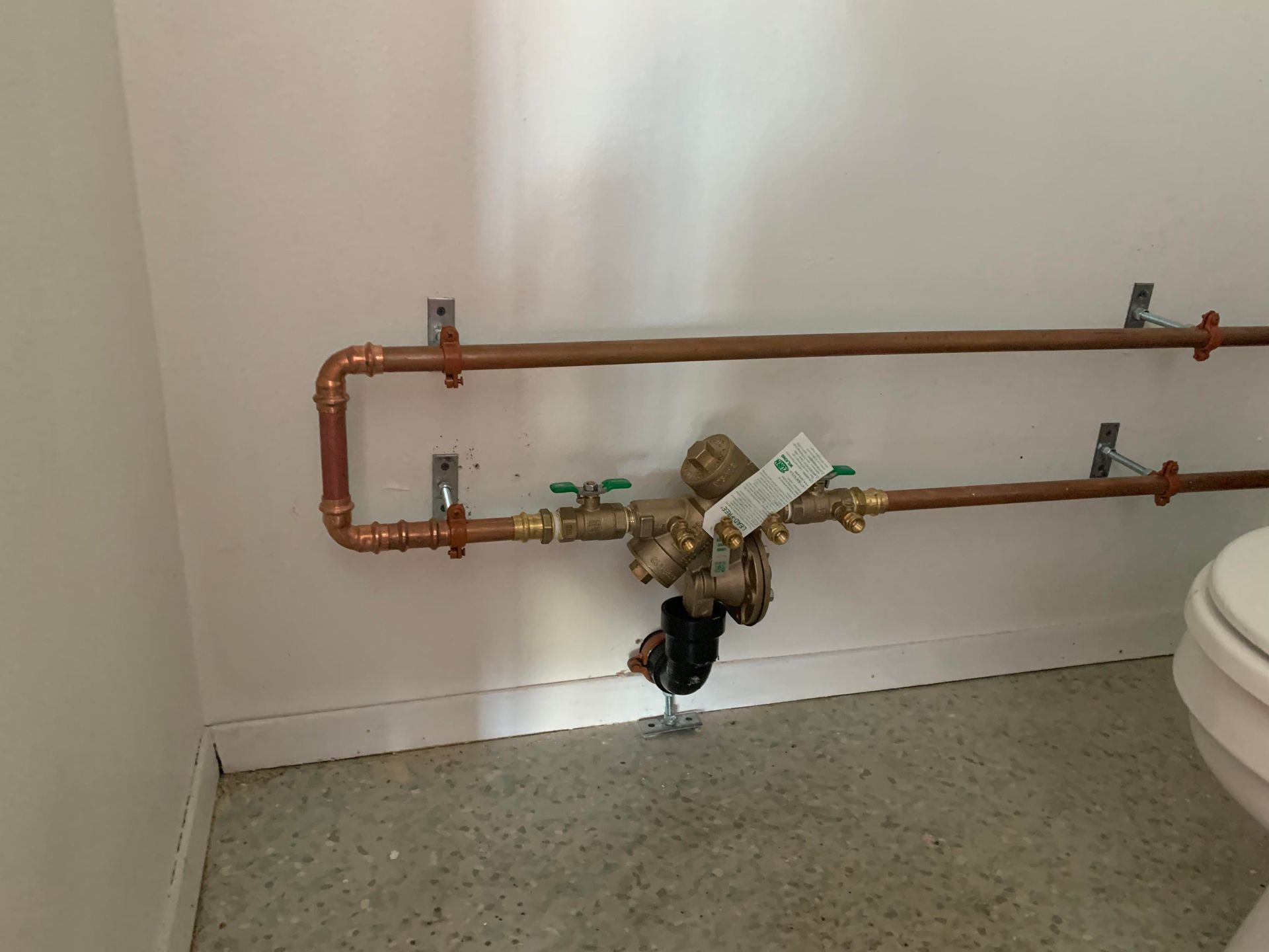 Copper plumbing pipes with a water valve in a white-walled bathroom.