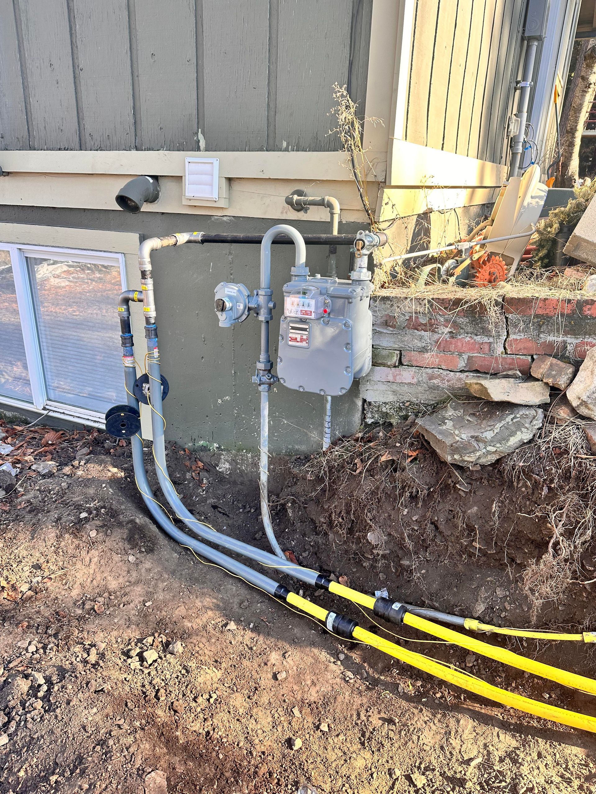 Gas meter attached to a building with buried yellow gas lines visible in a dirt trench.