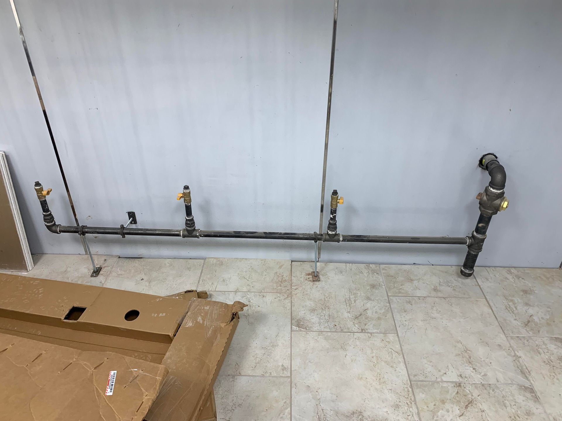 Gas pipes along a wall, with shut-off valves. Cardboard box on floor.