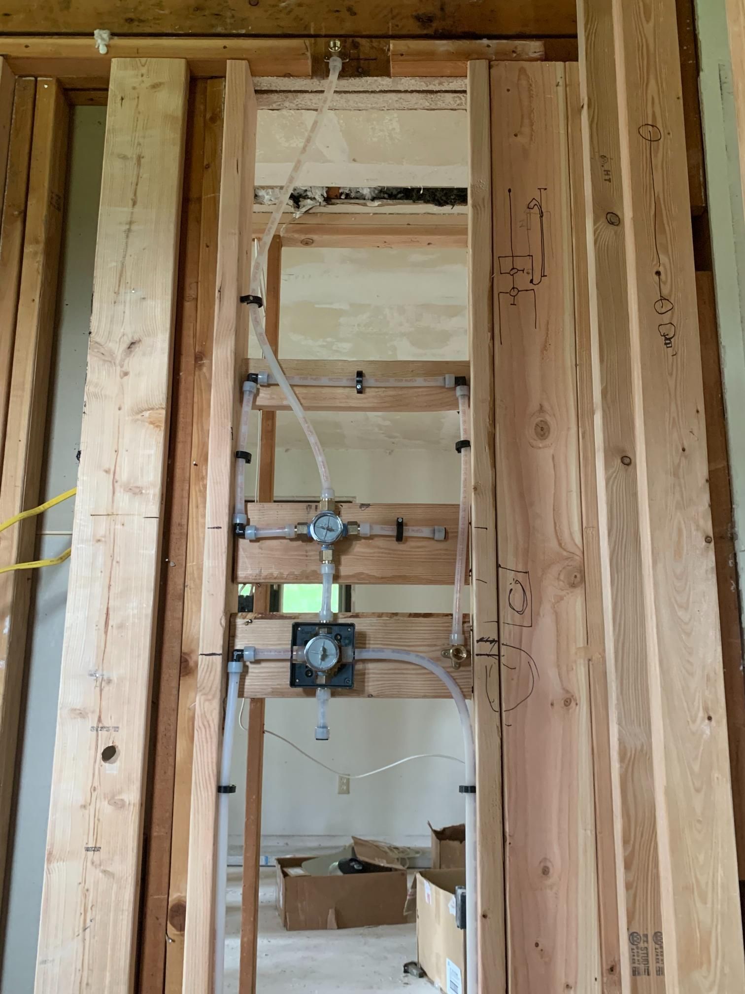 Framed wooden shower plumbing. Clear plastic pipes, silver fixtures against wood studs. Interior setting.