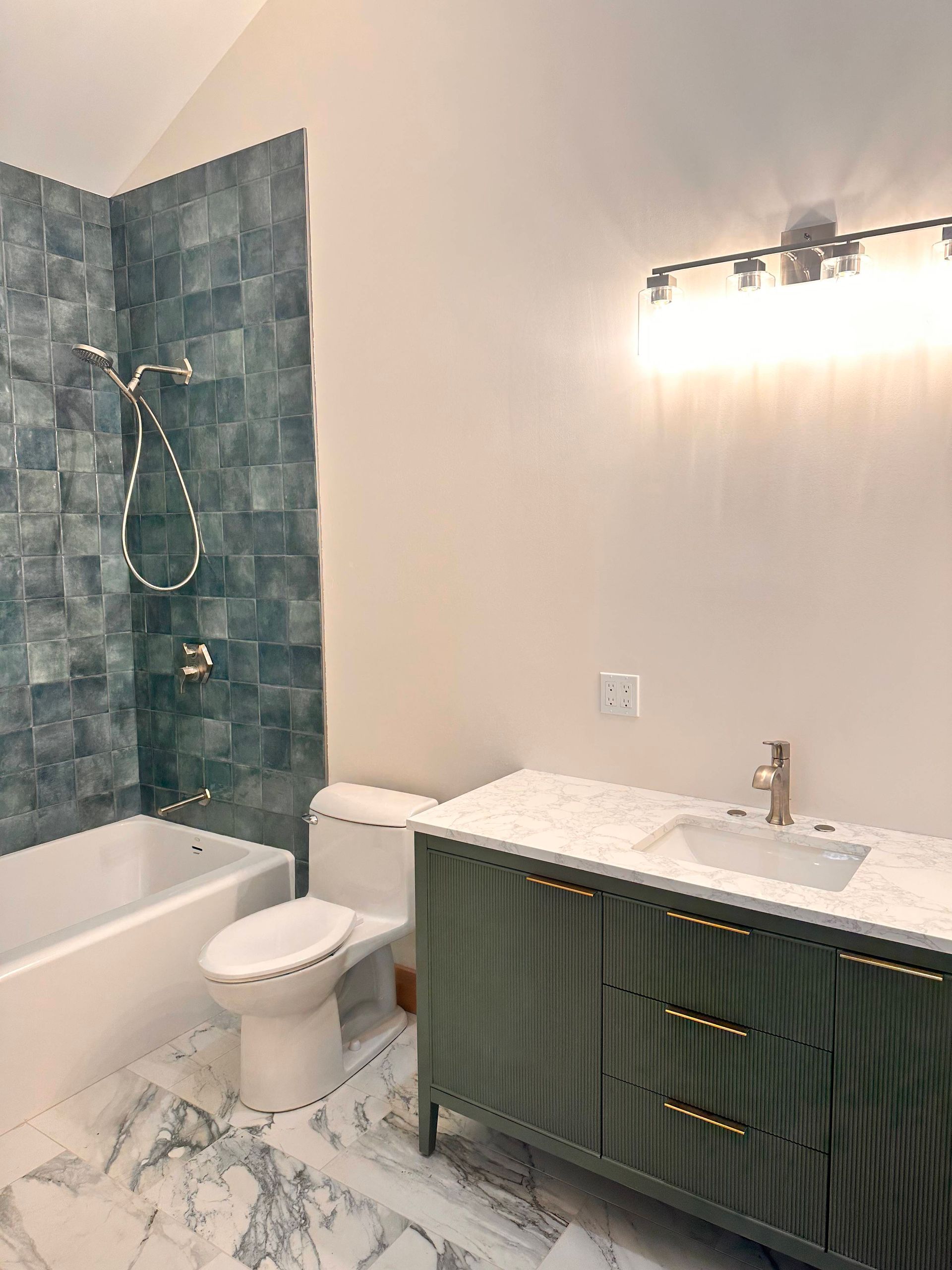 A modern bathroom featuring a white vanity with a marble countertop, a white toilet, and a bathtub with blue tile walls.