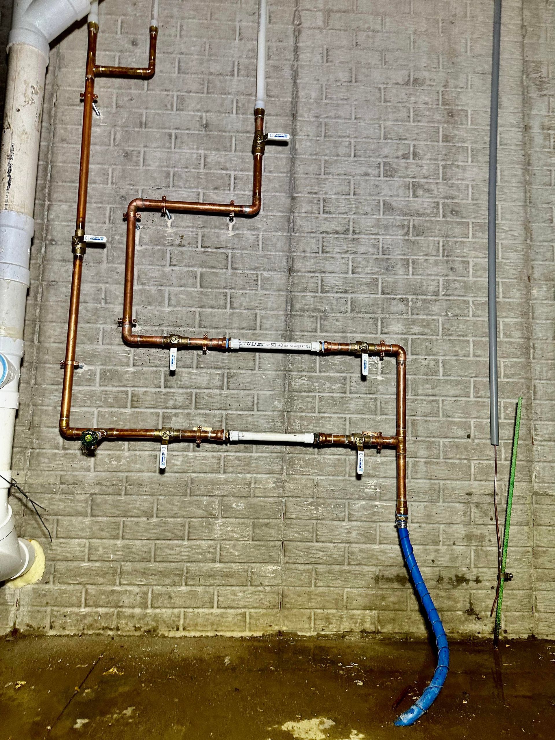 Copper plumbing pipes against a brick wall, with blue hose at the bottom.