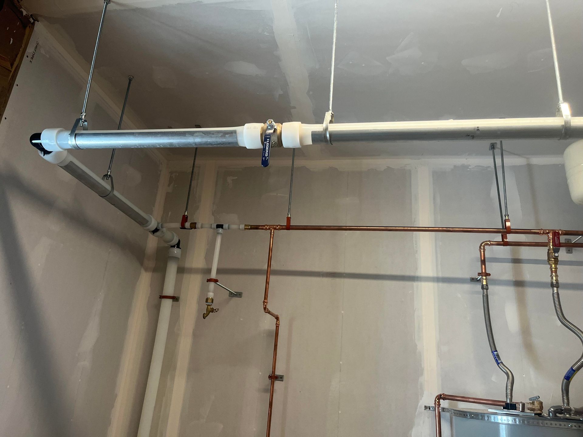 Pipes and valves in a utility room, attached to the ceiling. Copper and metal tubing, various fasteners.