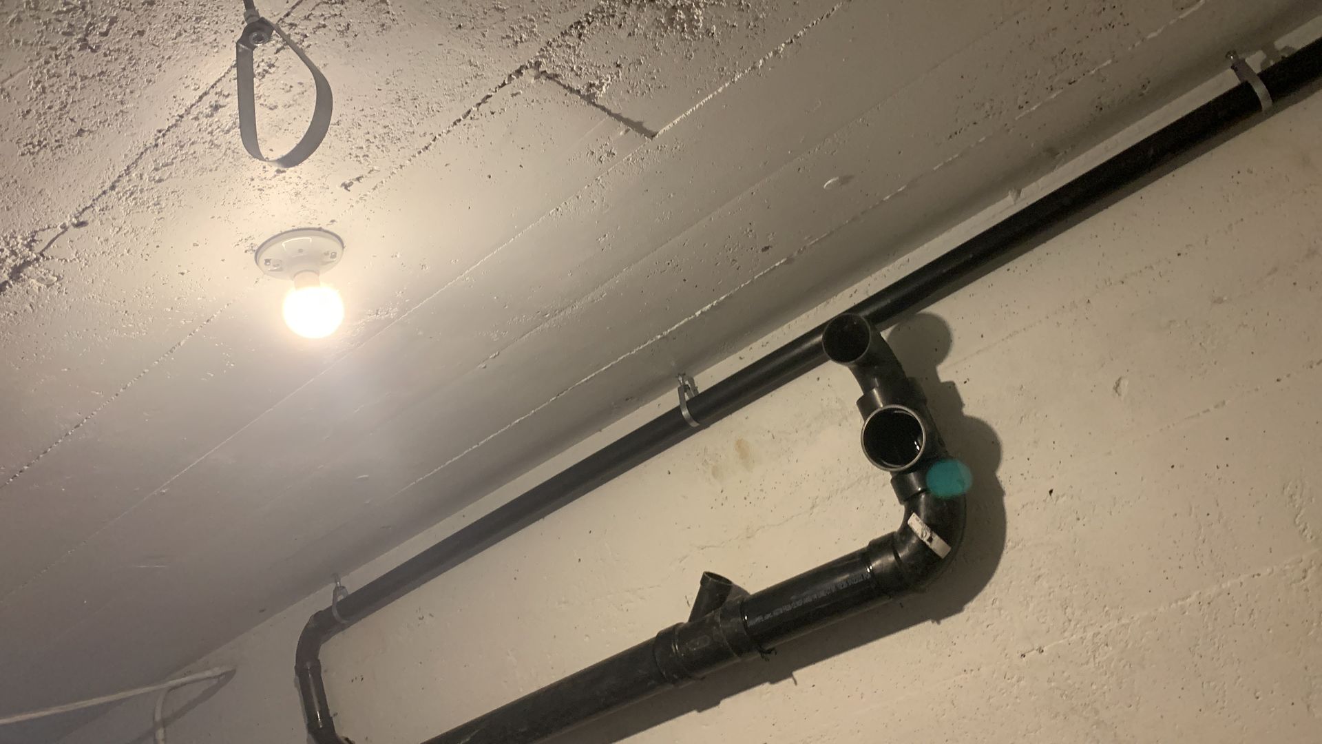 Black pipes on a white wall, lit by a ceiling light. A valve is visible.