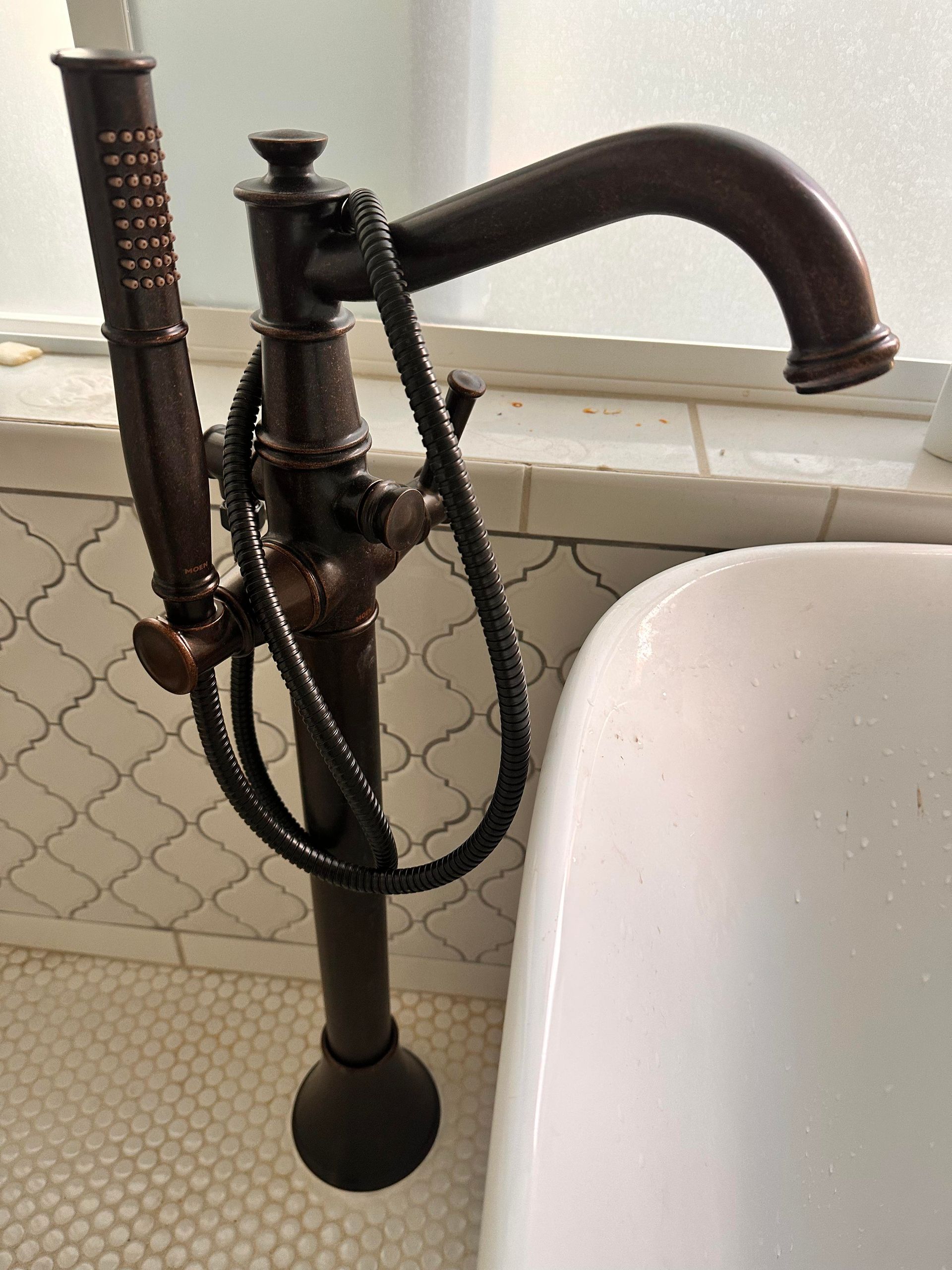 Bronze freestanding tub faucet with handheld shower next to a white tub.