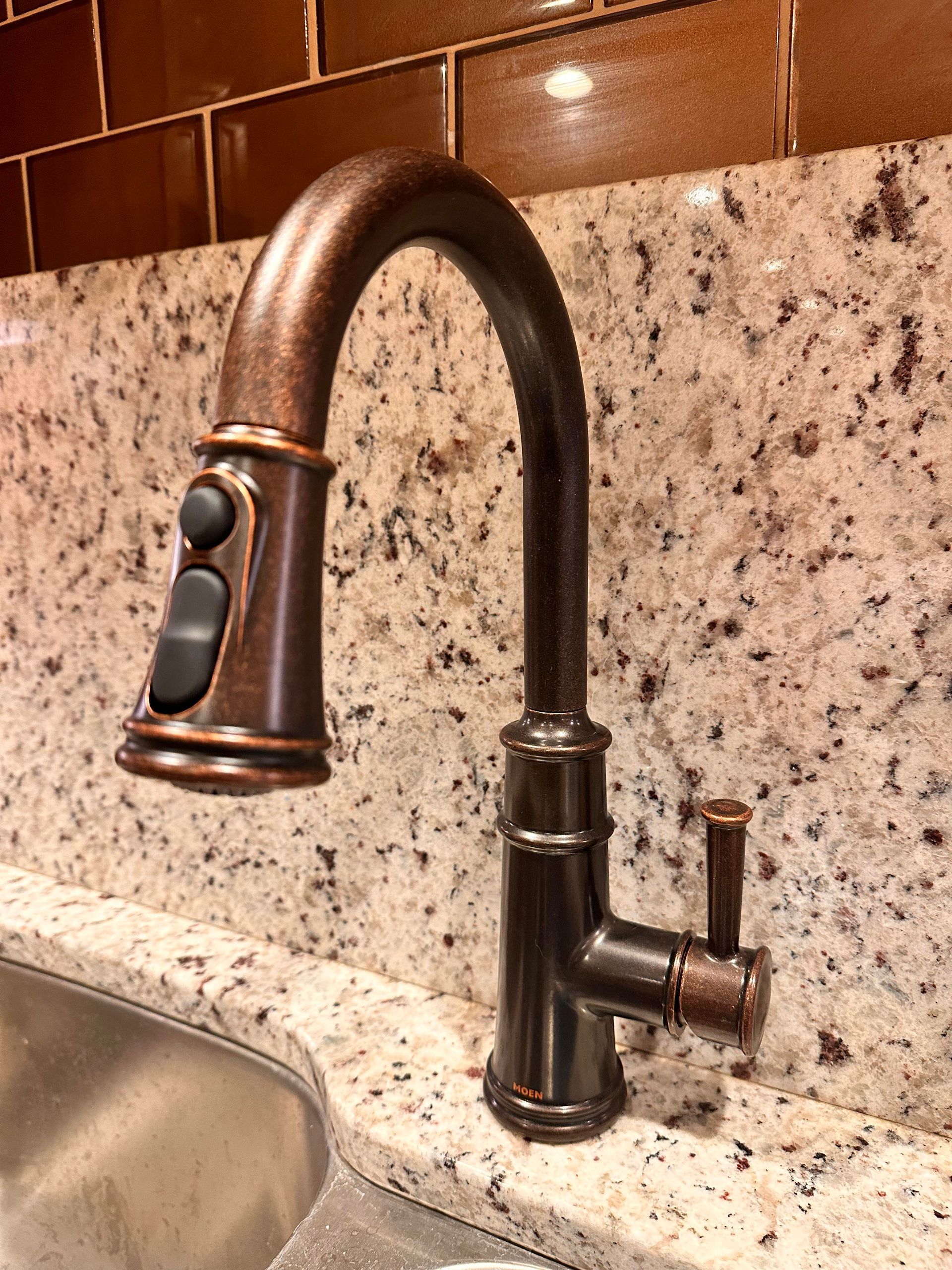 Bronze kitchen faucet with pull-down sprayer on a granite countertop.