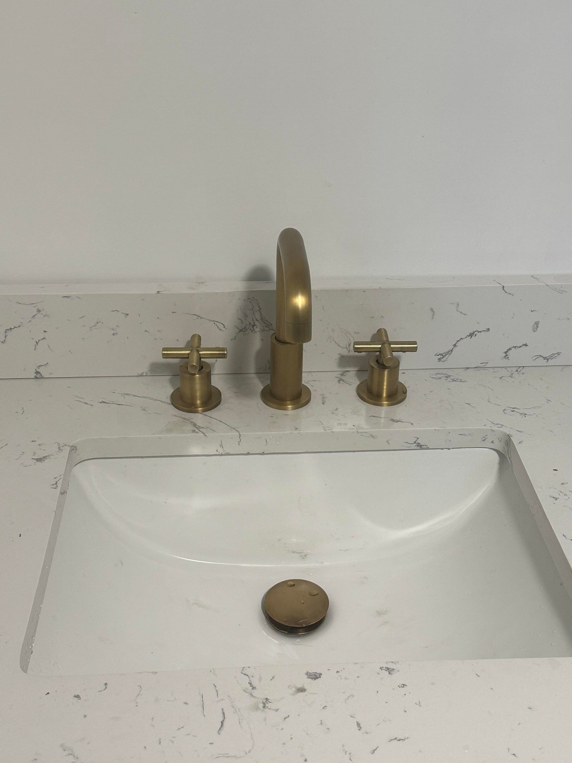 Gold faucet and cross-handle fixtures above a white sink in a bathroom.