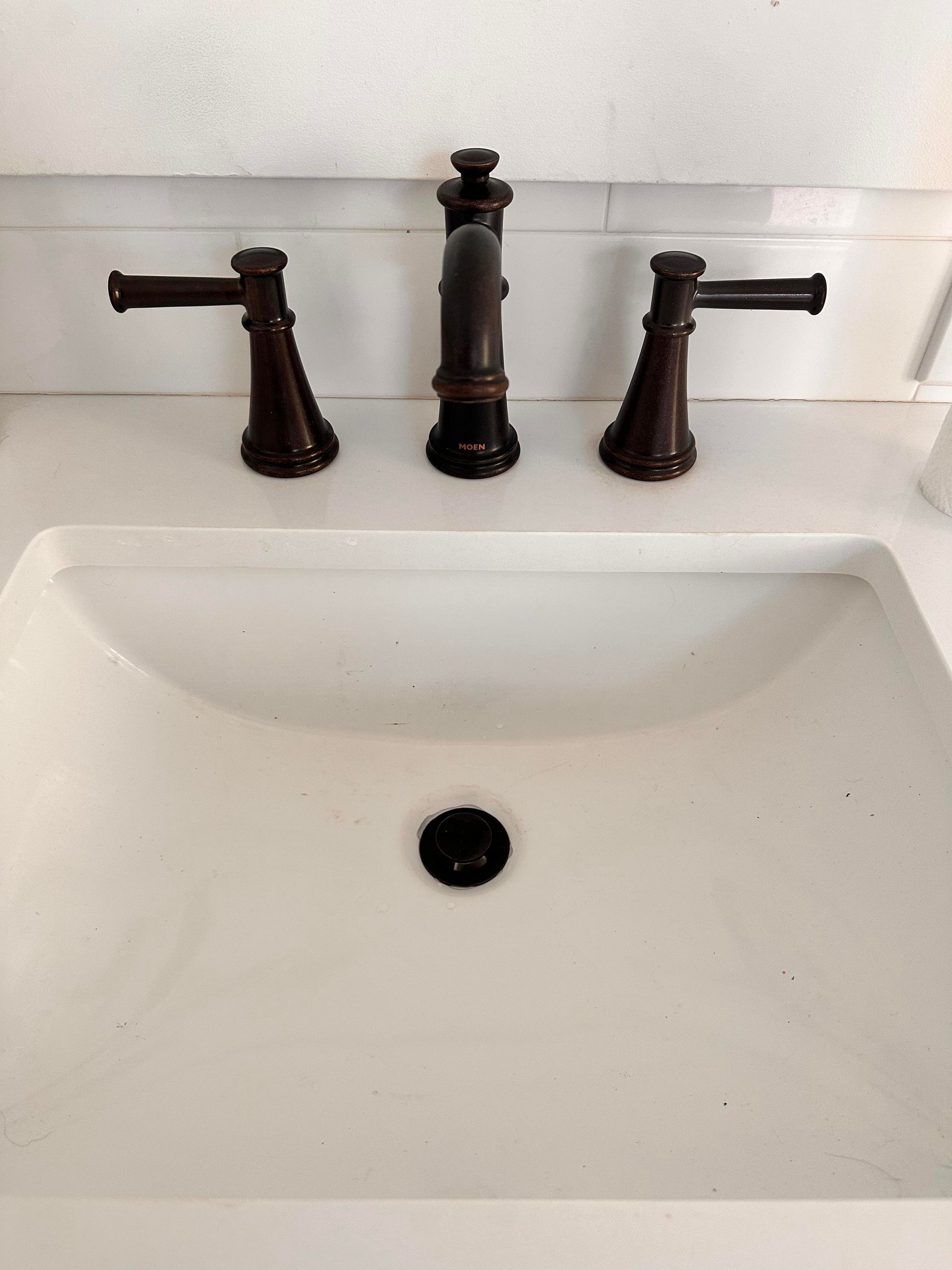 White sink with bronze faucet and handles.
