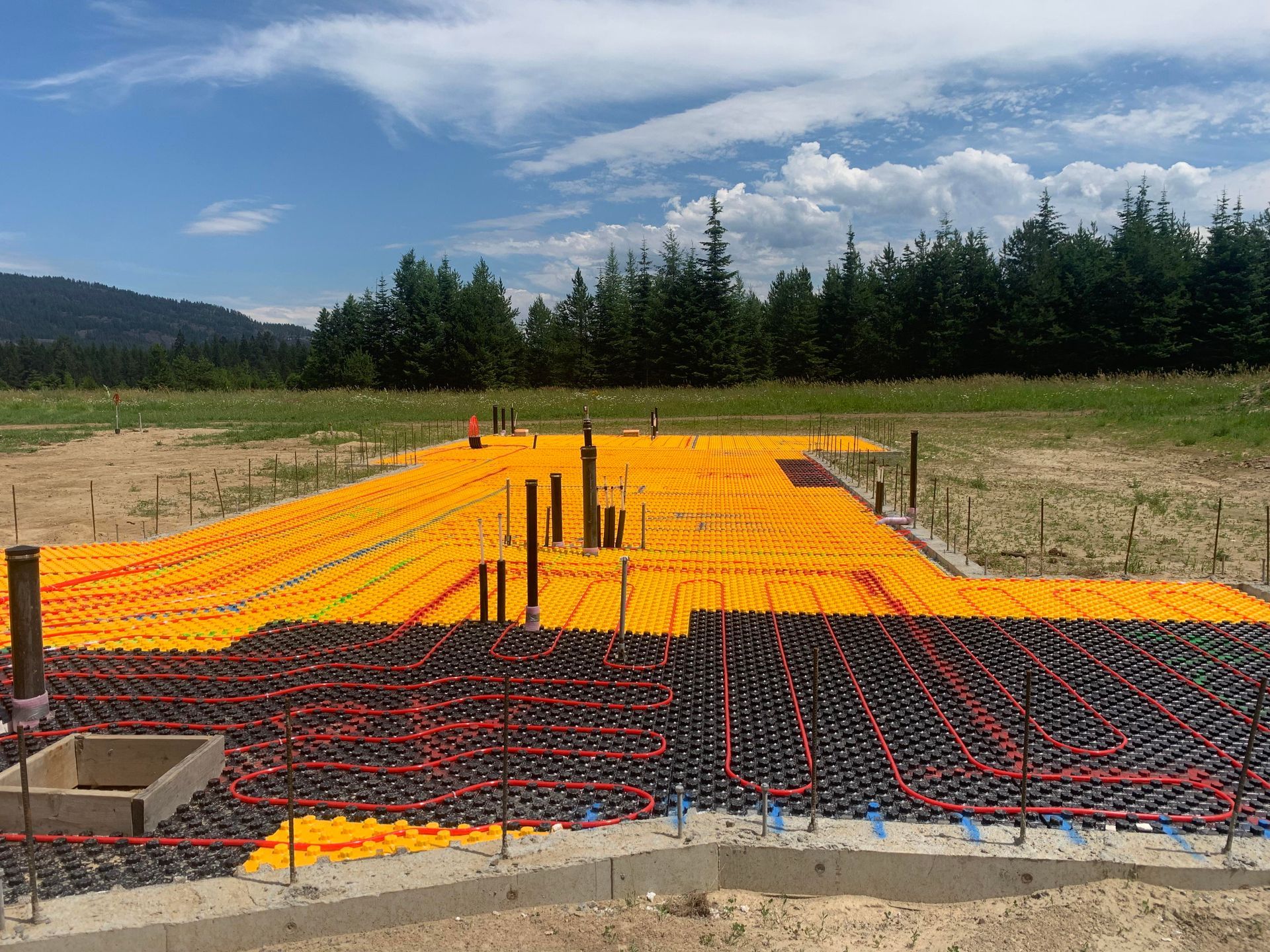 Orange and black radiant floor heating tubes laid on a concrete slab, prepared for construction in a field.