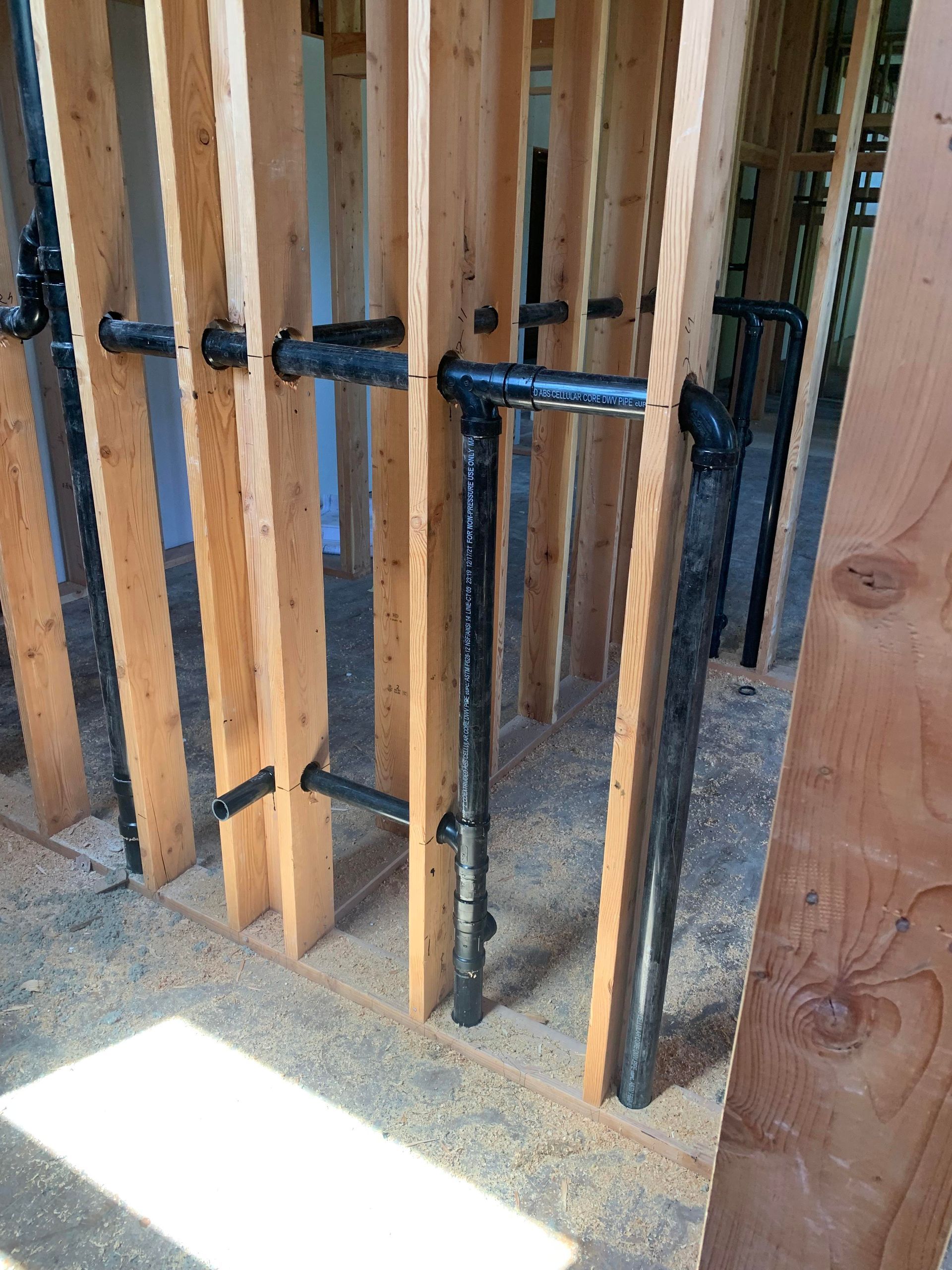 Wooden studs with black pipes, likely for plumbing, running through them; construction site.